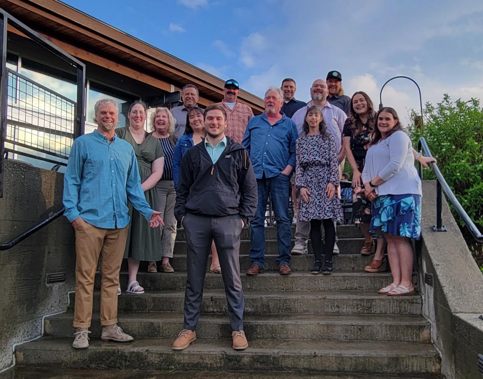 Group of people smiling on outdoor stairs under a blue sky.