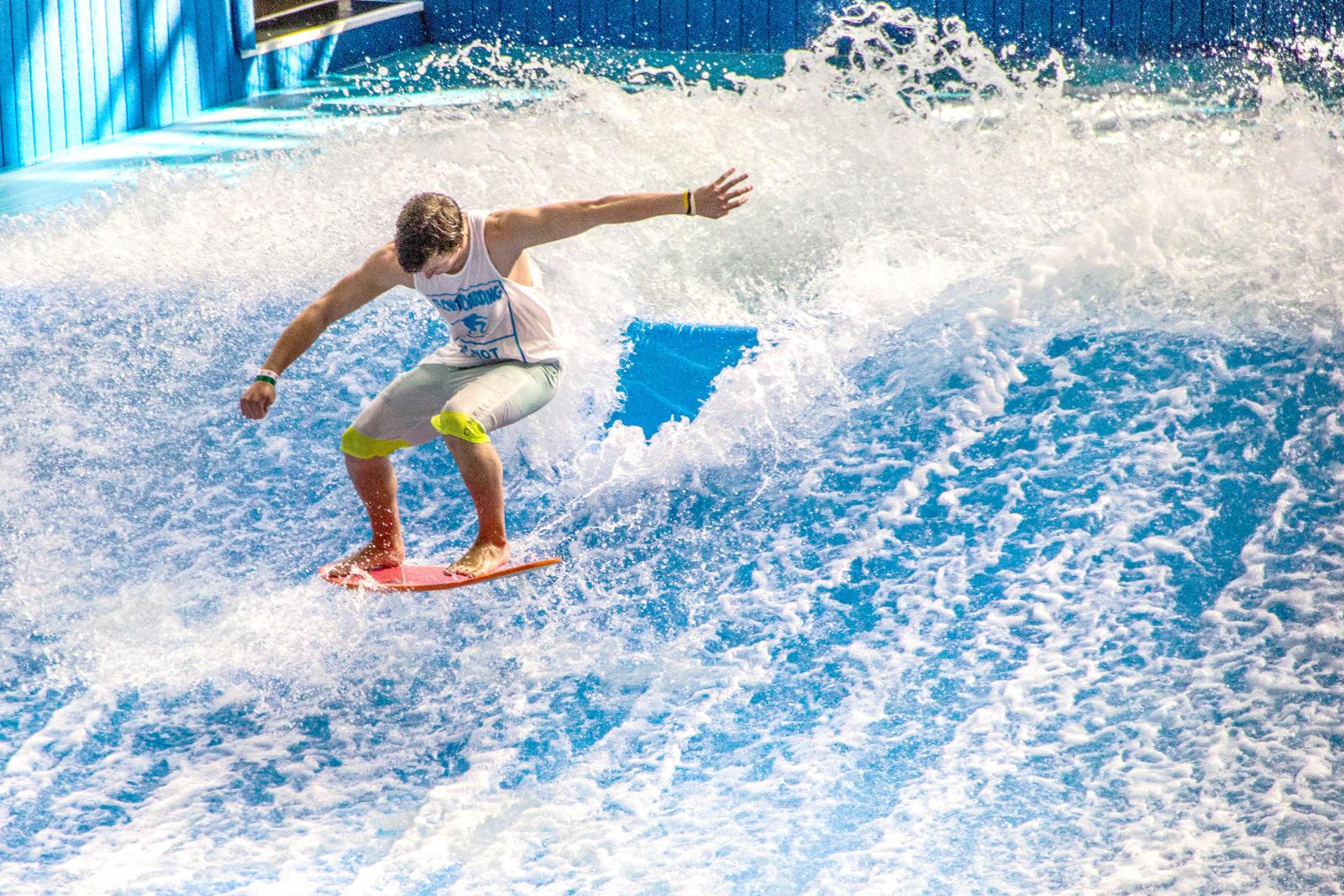 Surfer balancing on artificial wave in bright sunlight.