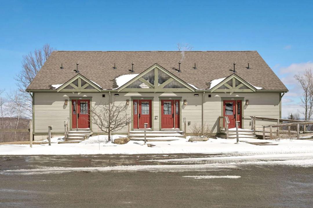 Two-story building with red doors, snow on the ground, clear blue sky.