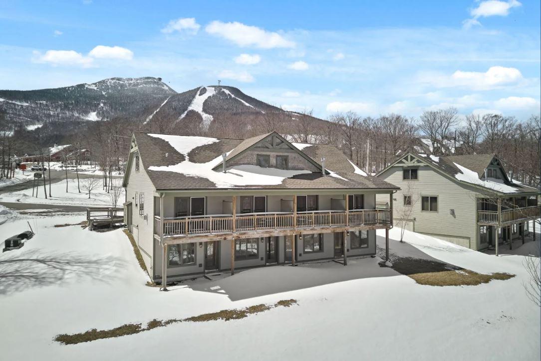 Snow-covered house with a mountain backdrop under a blue sky.