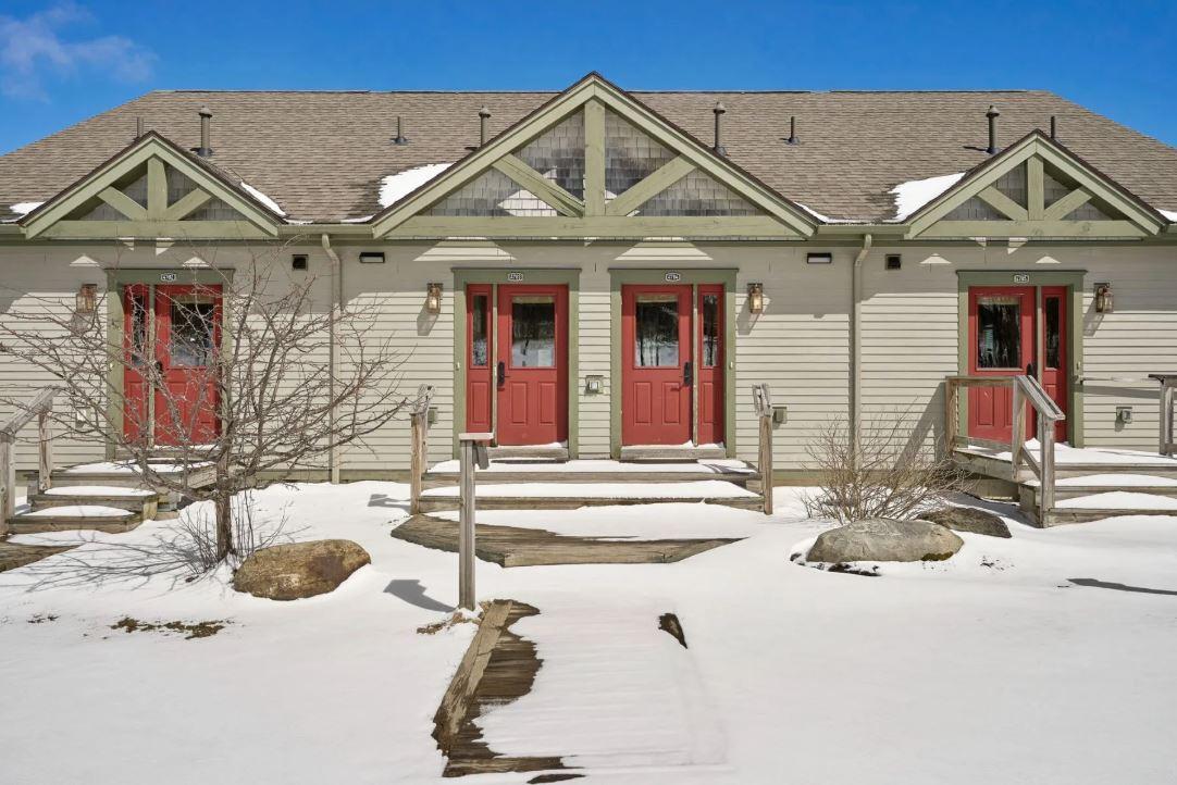 Snow-covered pathway leading to a house with red doors and a sloped roof.
