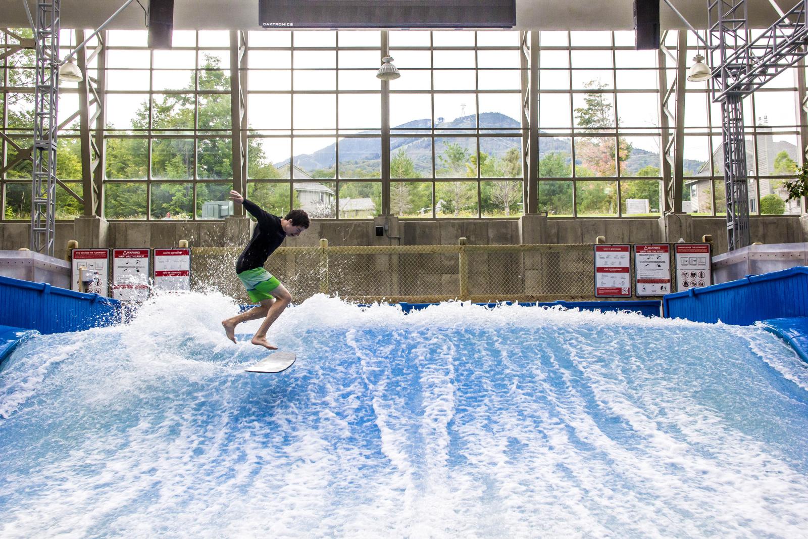 Indoor wave surfing, man in green shorts balancing on surfboard.