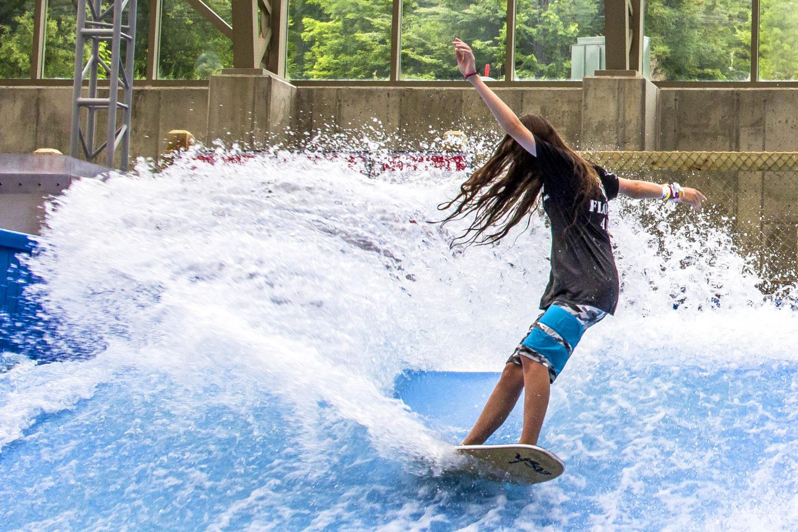 Surfer balancing on an indoor wave, surrounded by splashing water.