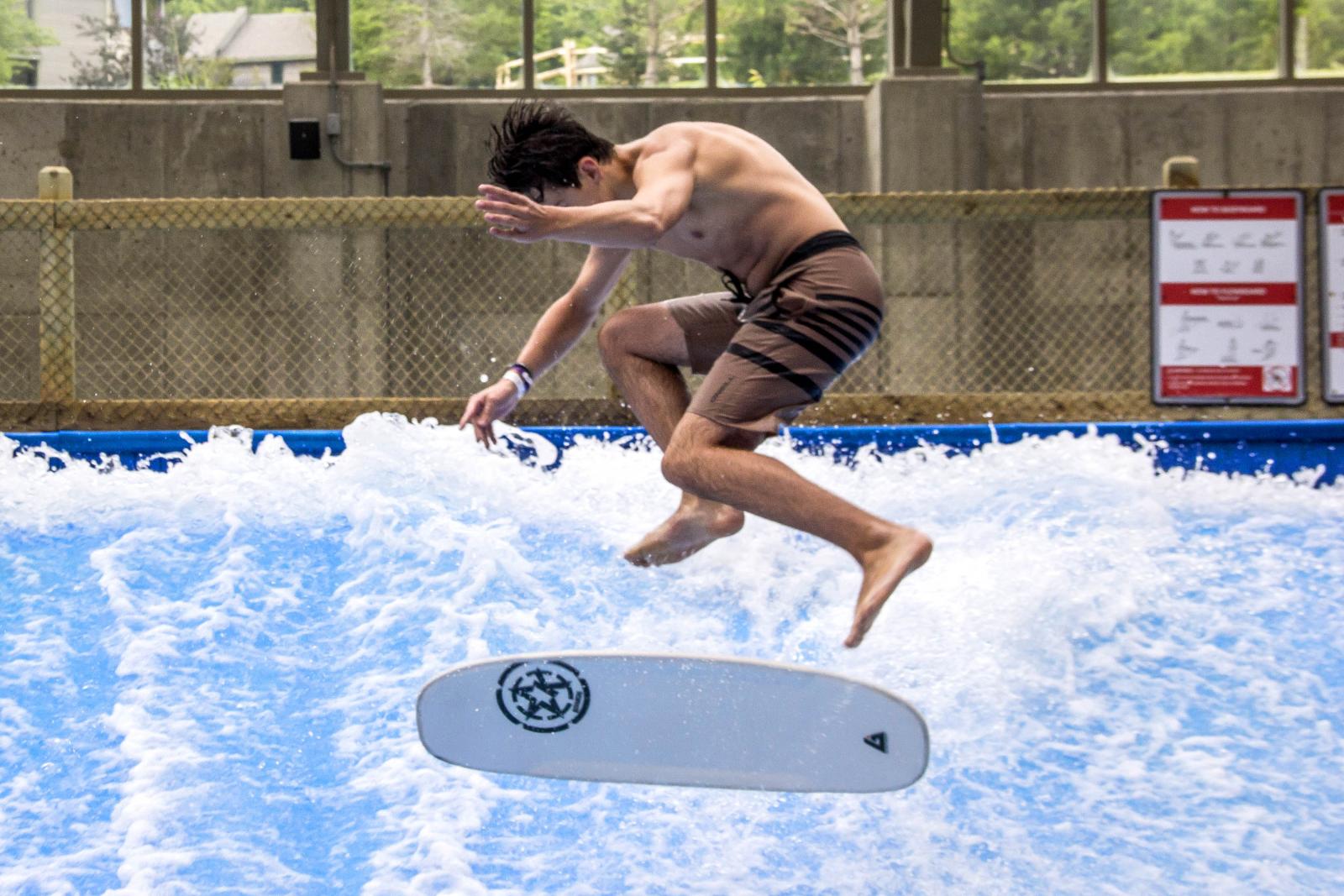 Man jumping mid-air on indoor surfing wave, board below.