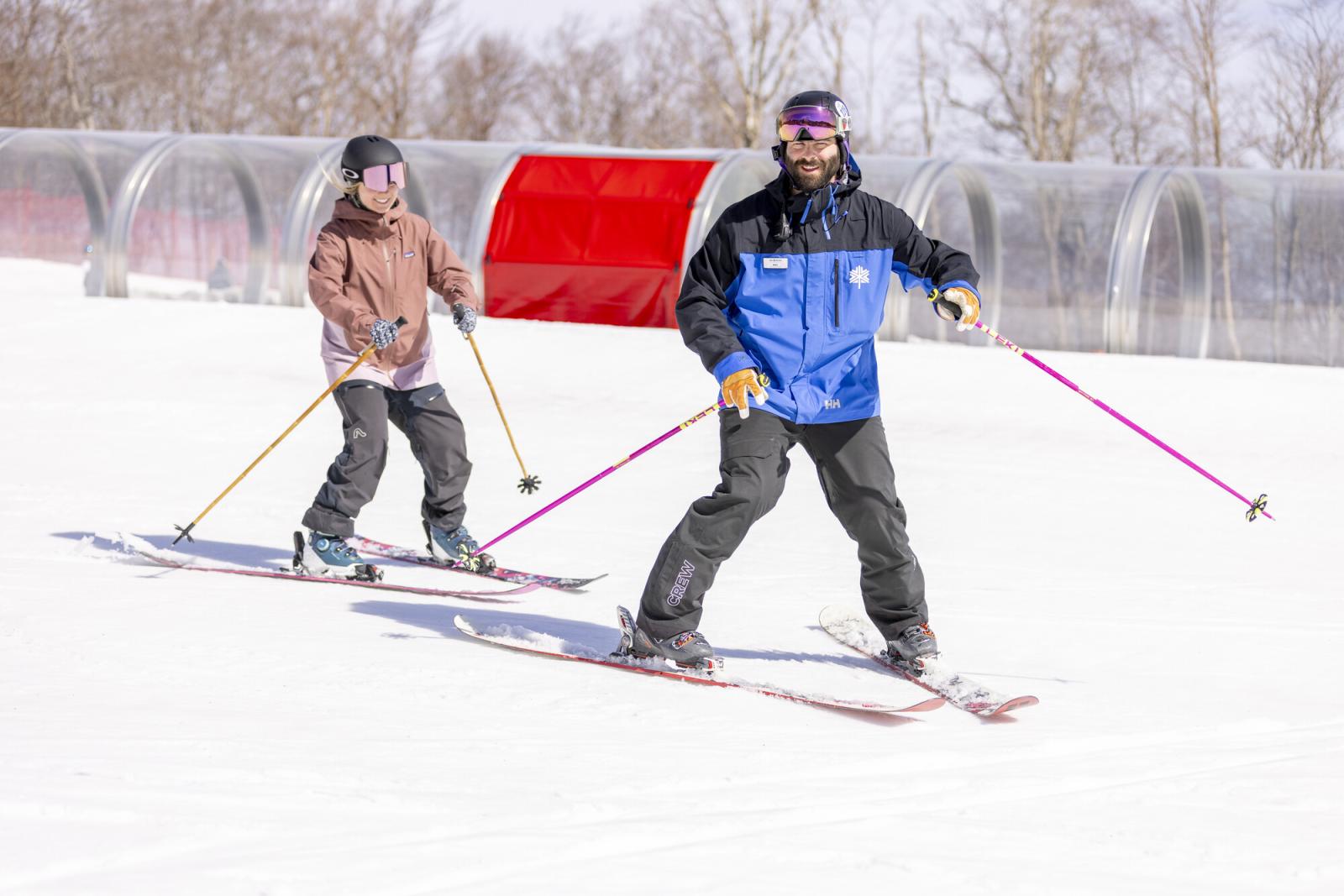 Two people skiing on a snowy slope, one in a blue jacket instructing.