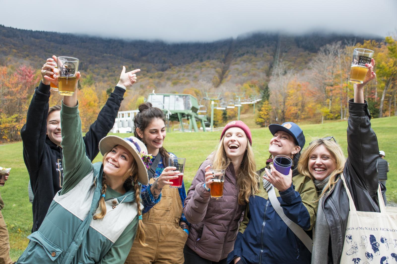 Group of friends smiling and raising glasses outdoors in a colorful autumn setting.