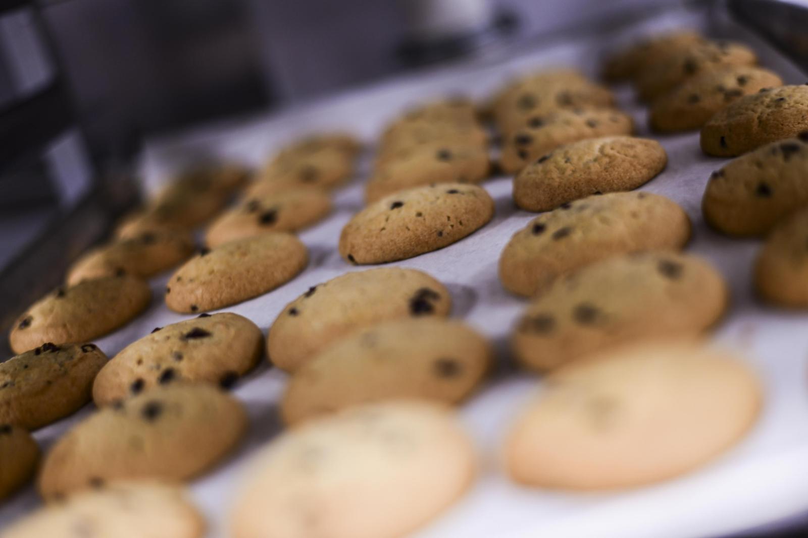 Freshly baked cookies on a tray, some with chocolate chips.