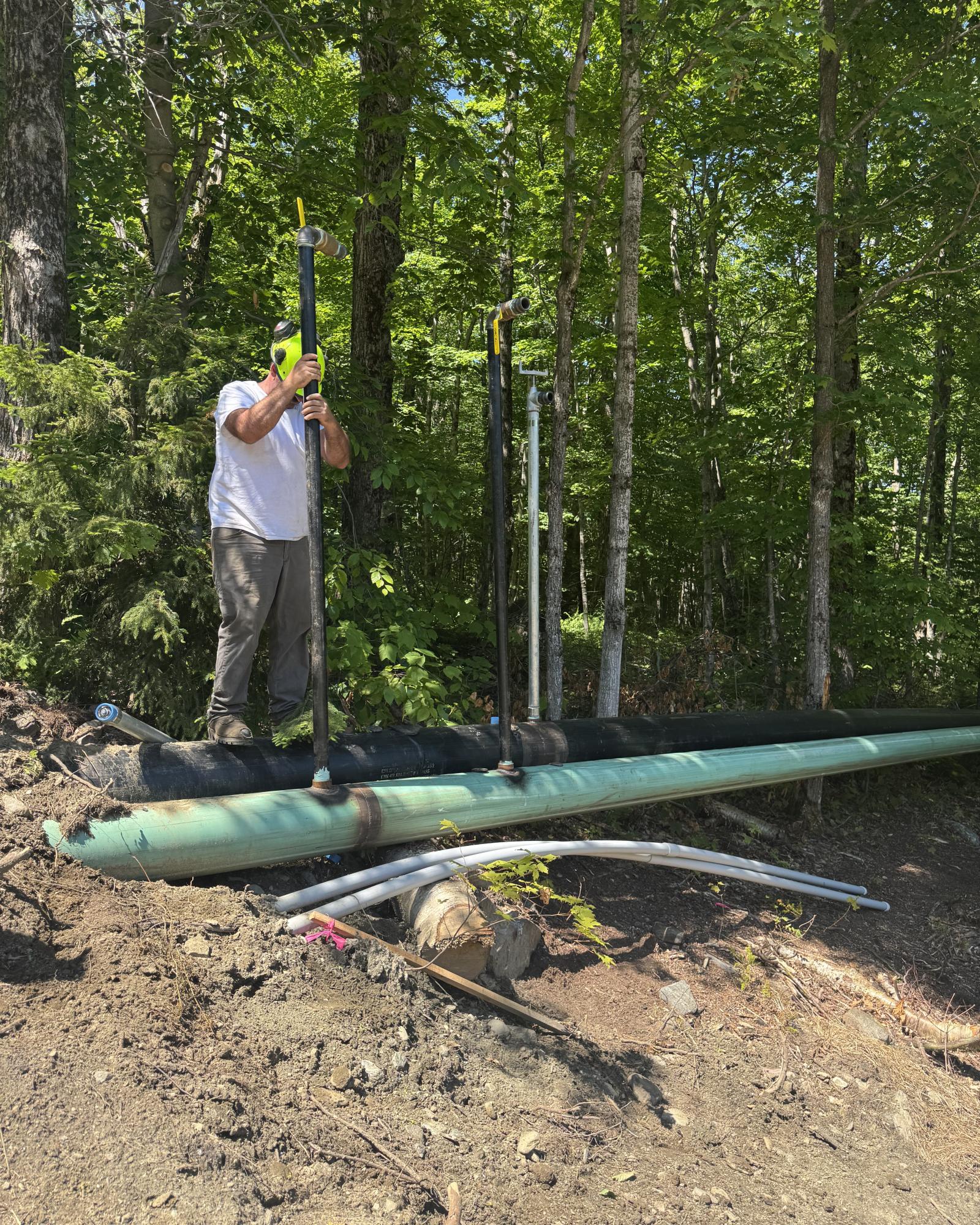 Snowmaker working snowmaking hydrant a forested area on a sunny day.