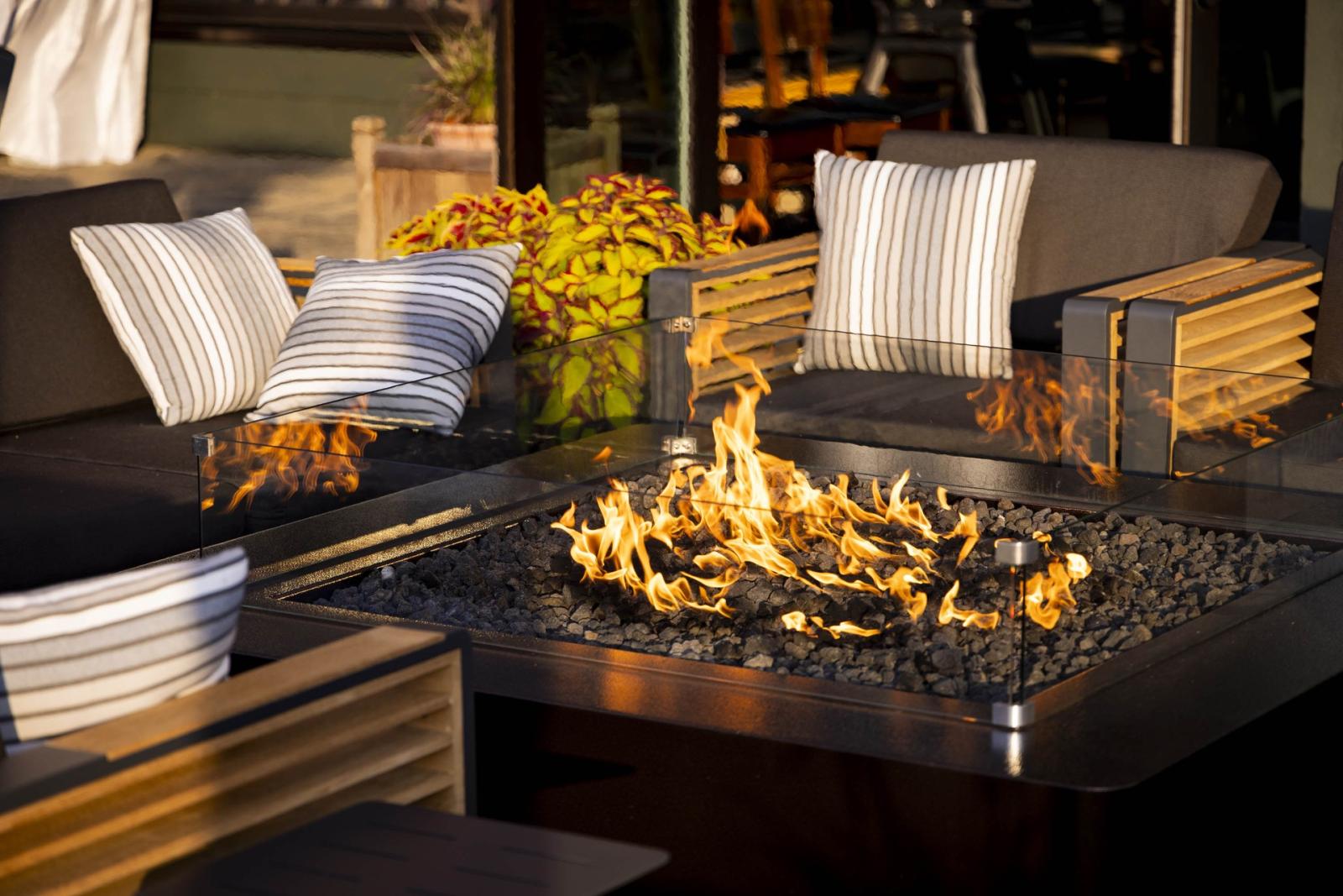 Fire pit with flames surrounded by striped cushions on sofas.