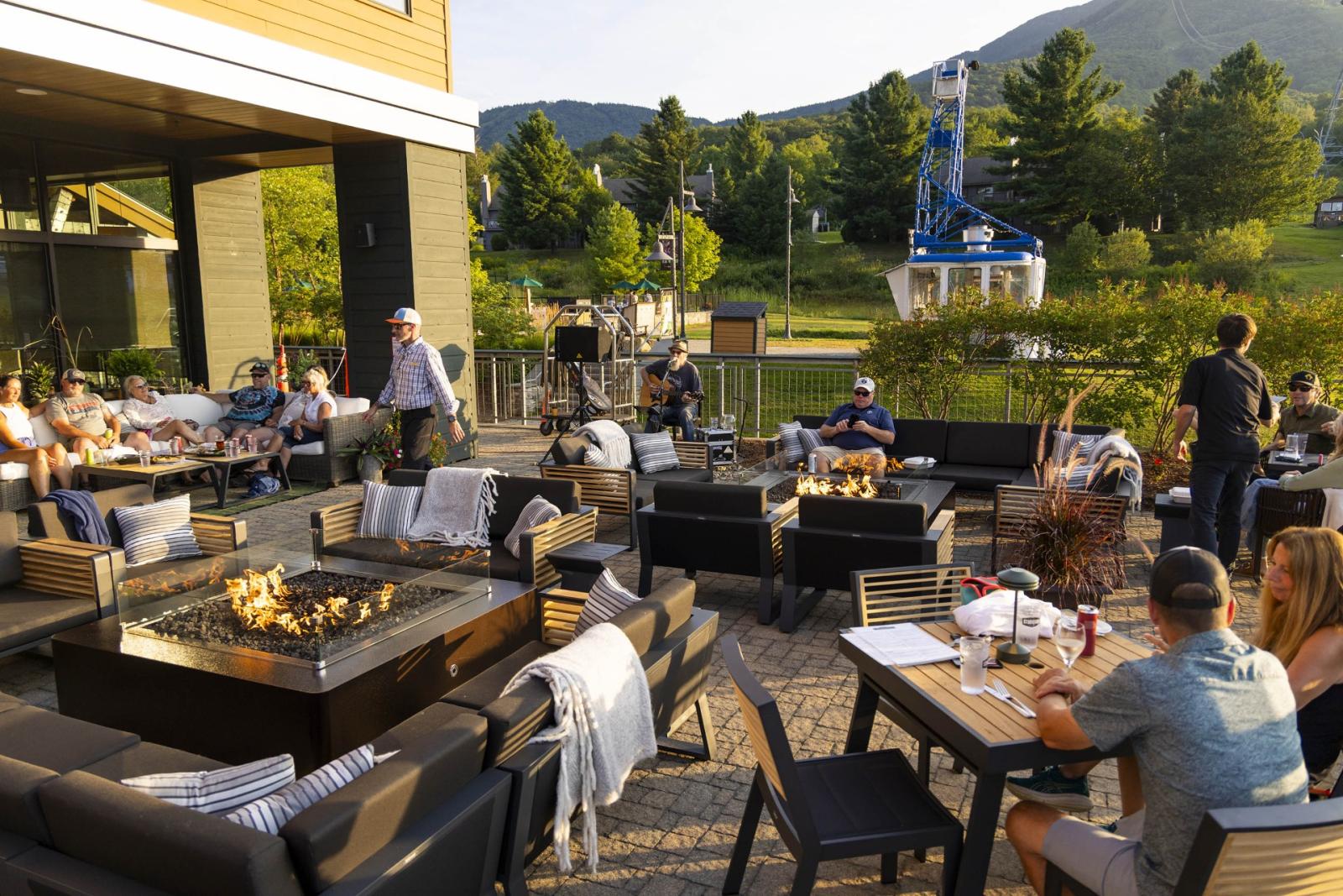 Outdoor patio with people dining, mountains and green trees in the background.