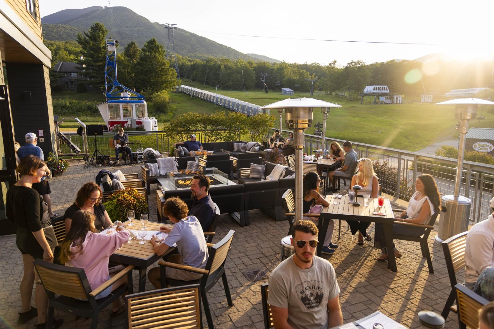 People dining on a patio with mountain views at sunset.