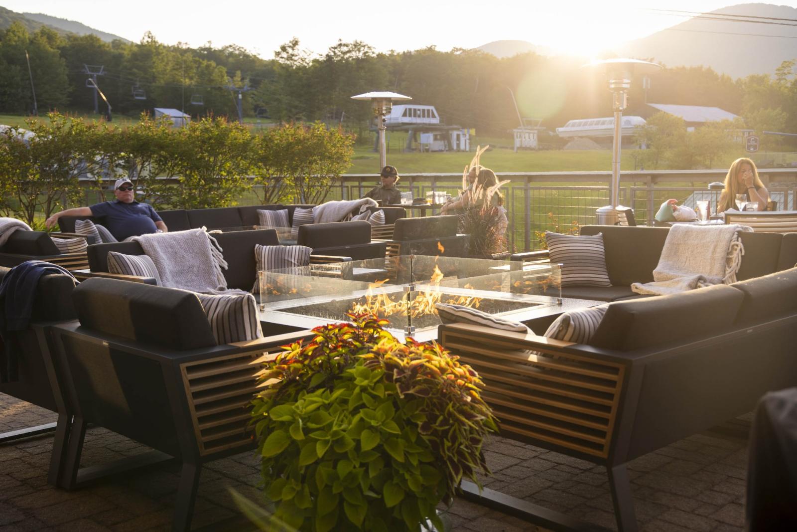 Outdoor patio with seating, fire pit, and mountain view at sunset.
