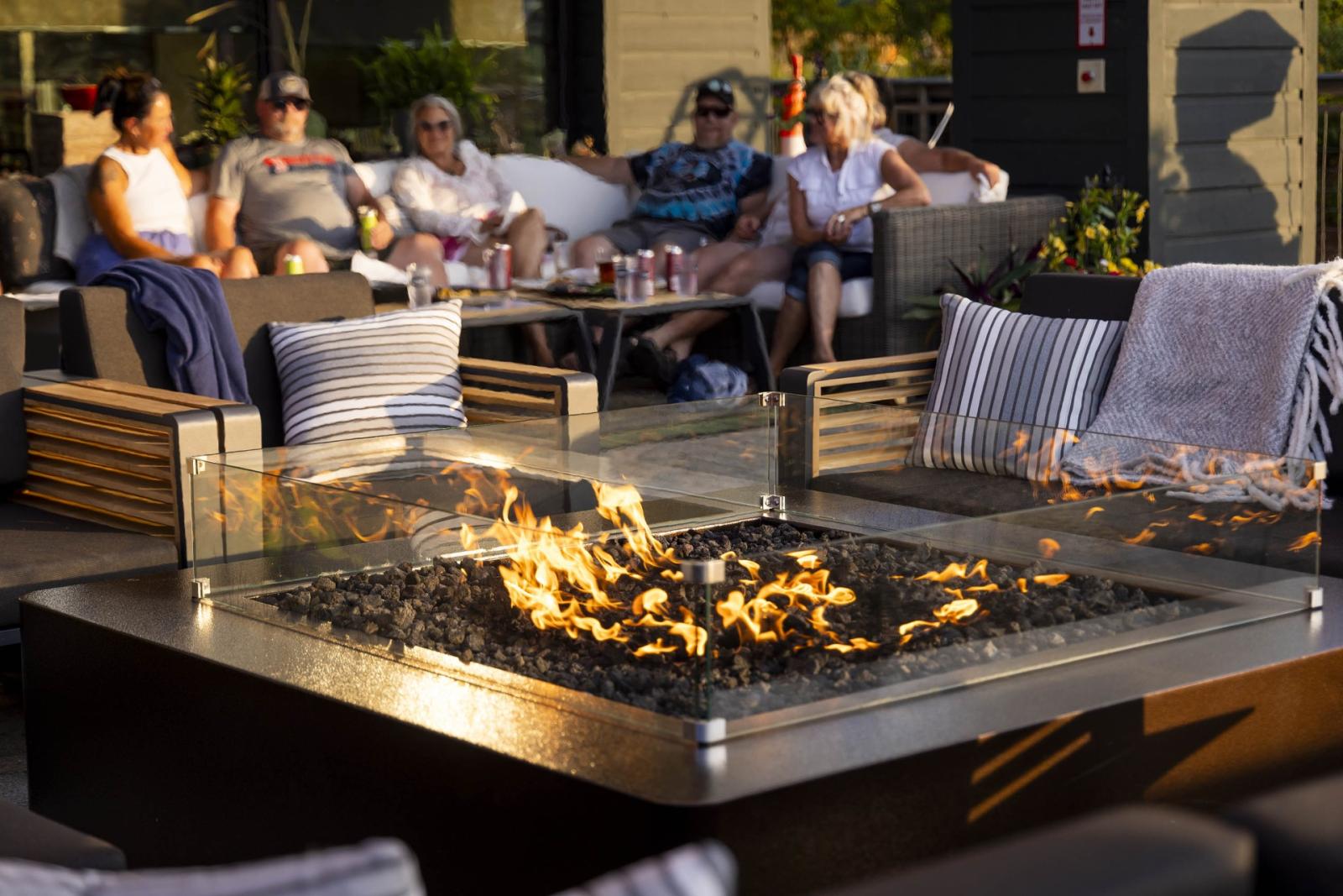 Outdoor lounge with fire pit and several people seated on couches.