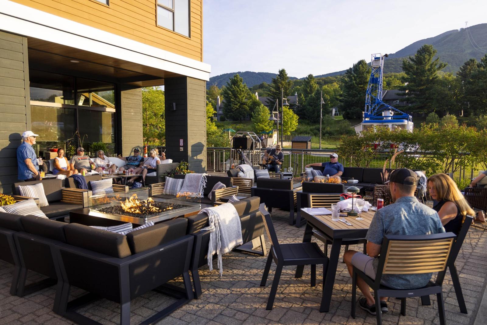 Outdoor patio dining with people relaxing, surrounded by trees and mountains.