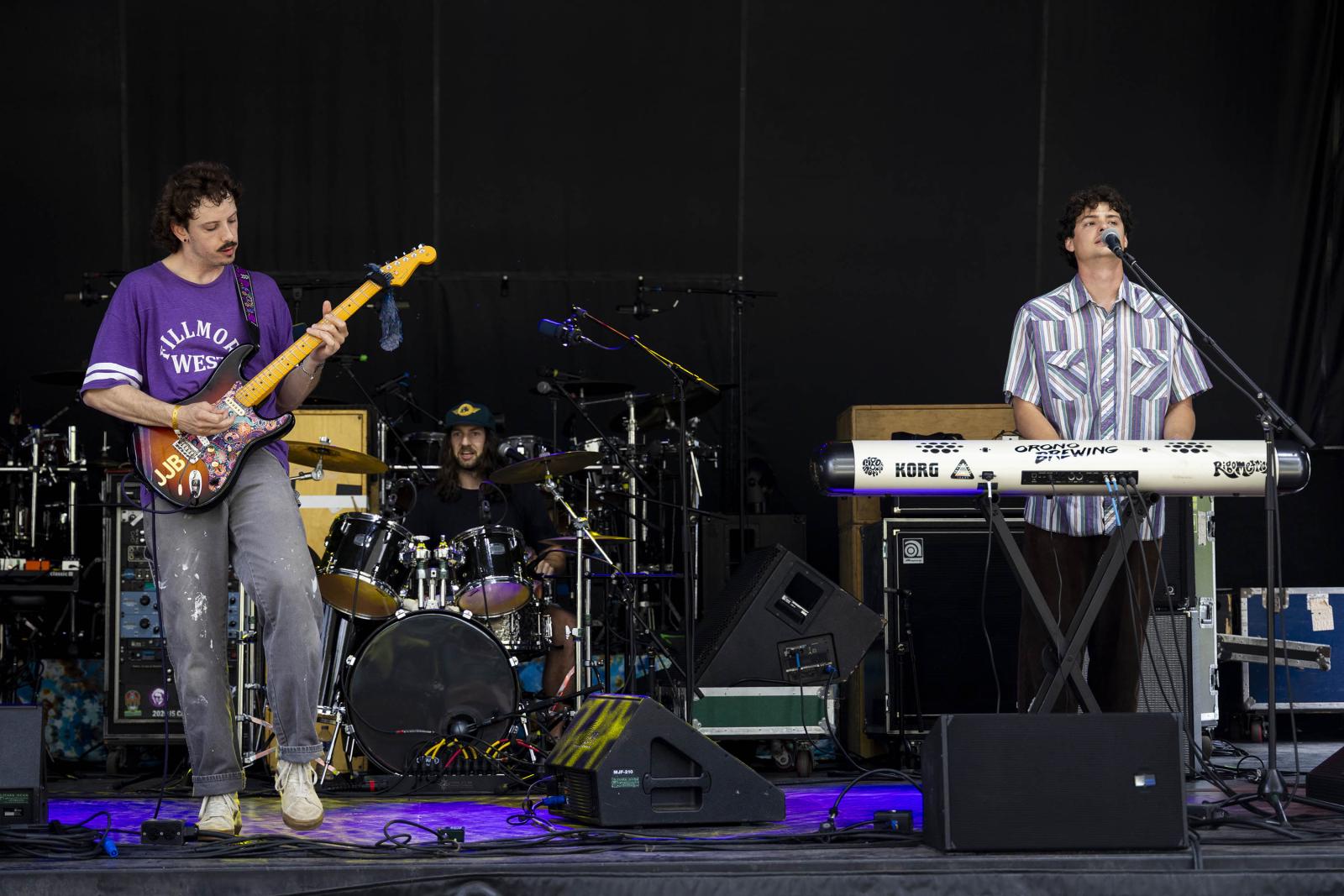 Band performing onstage with guitar, drums, and keyboard.