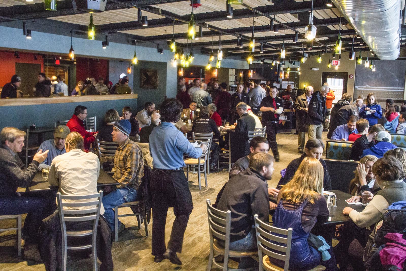 Crowded cafe with people sitting at tables, chatting and drinking.