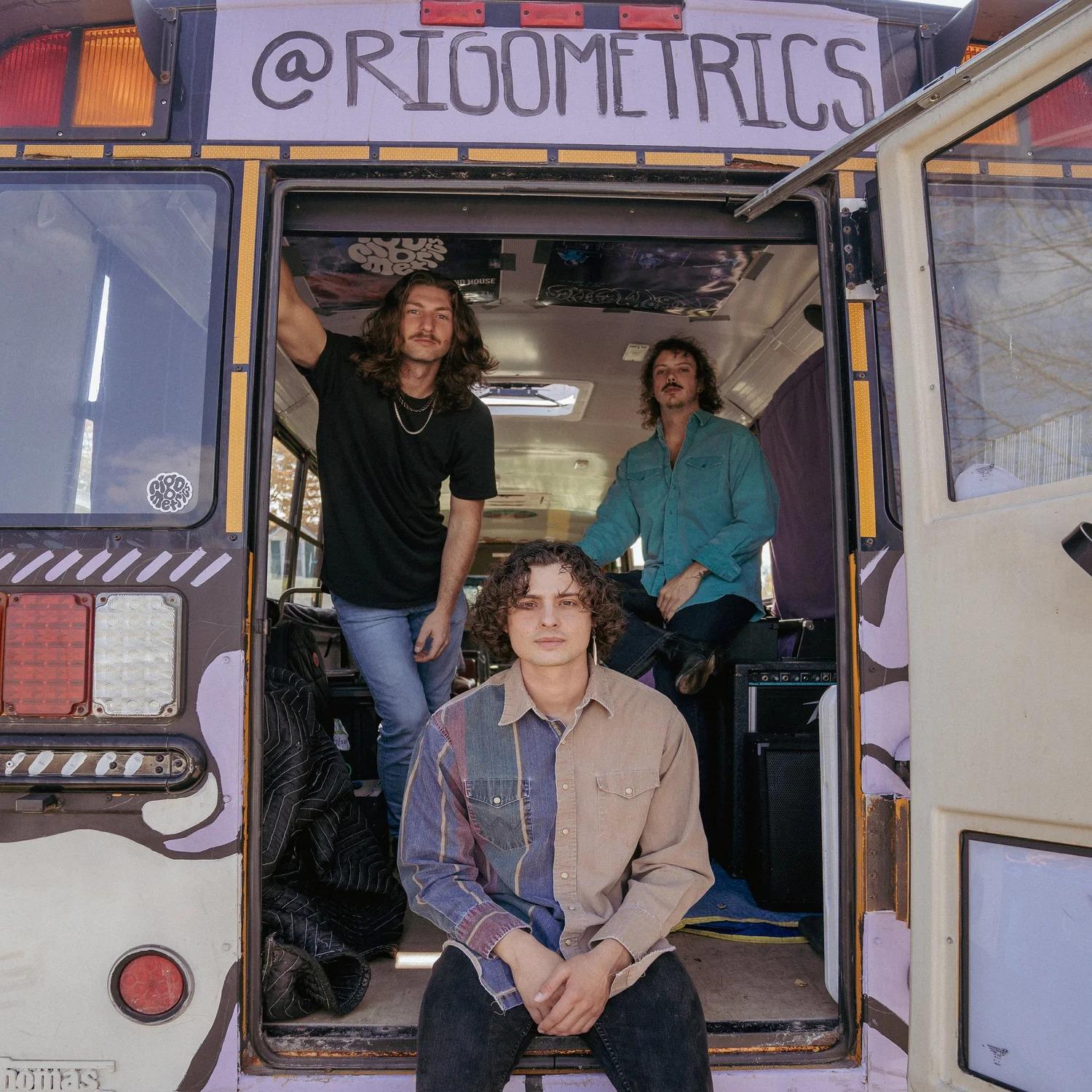 Three people smiling inside and at the back of a bus with colorful interior.
