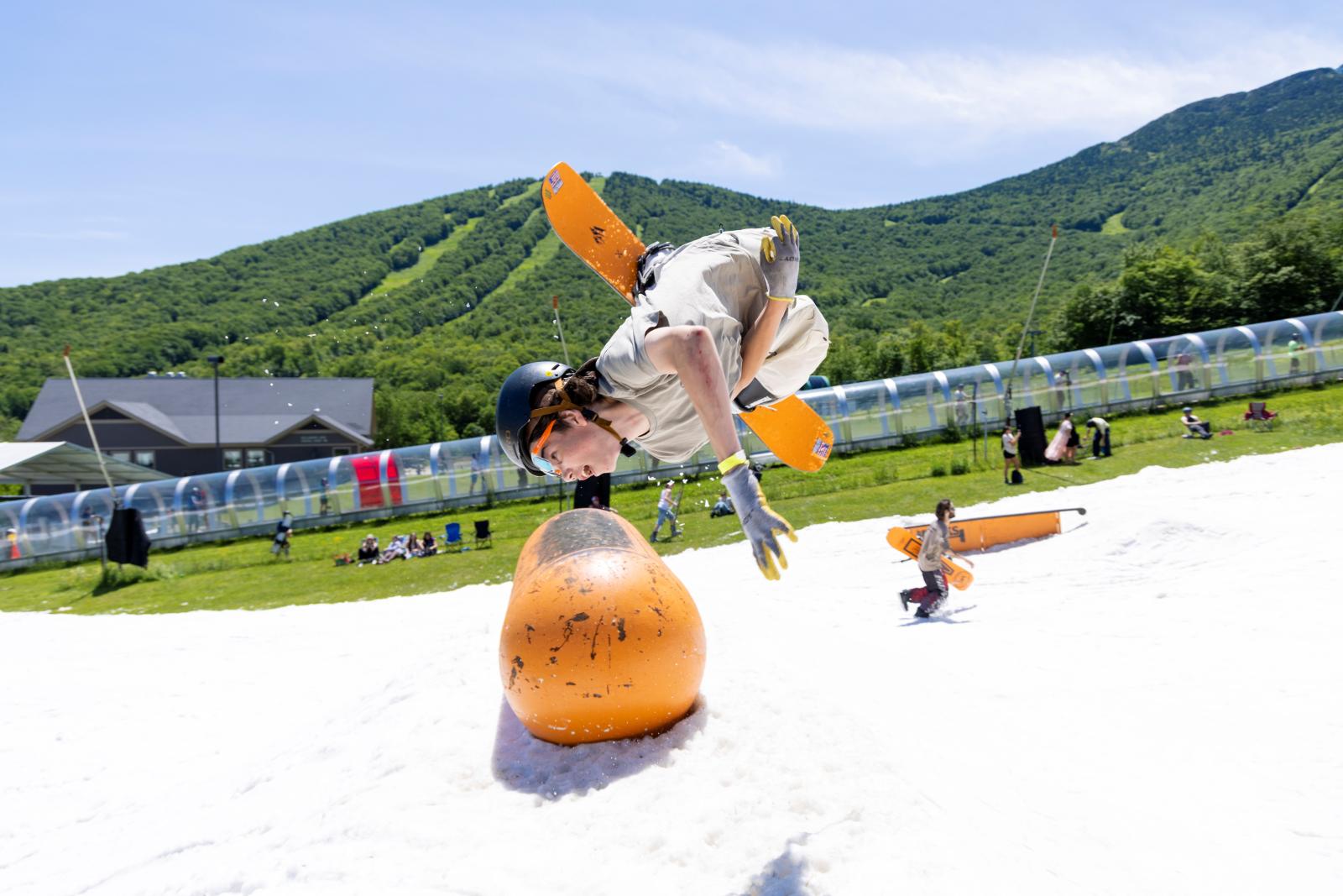 Child with helmet and toy airplane wings performs flip on snow-covered hill.
