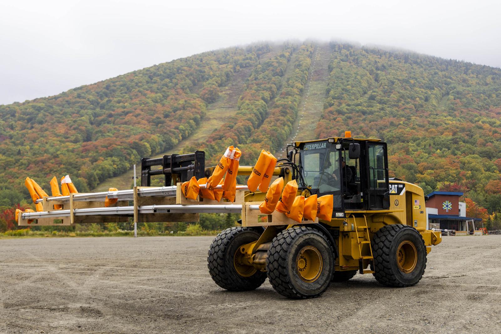 Yellow loader carrying orange objects in front of a forested hillside.