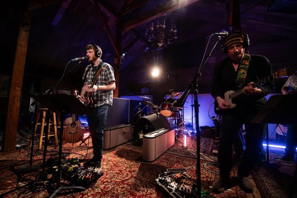 Band performing in a dimly lit venue with guitars and microphones.