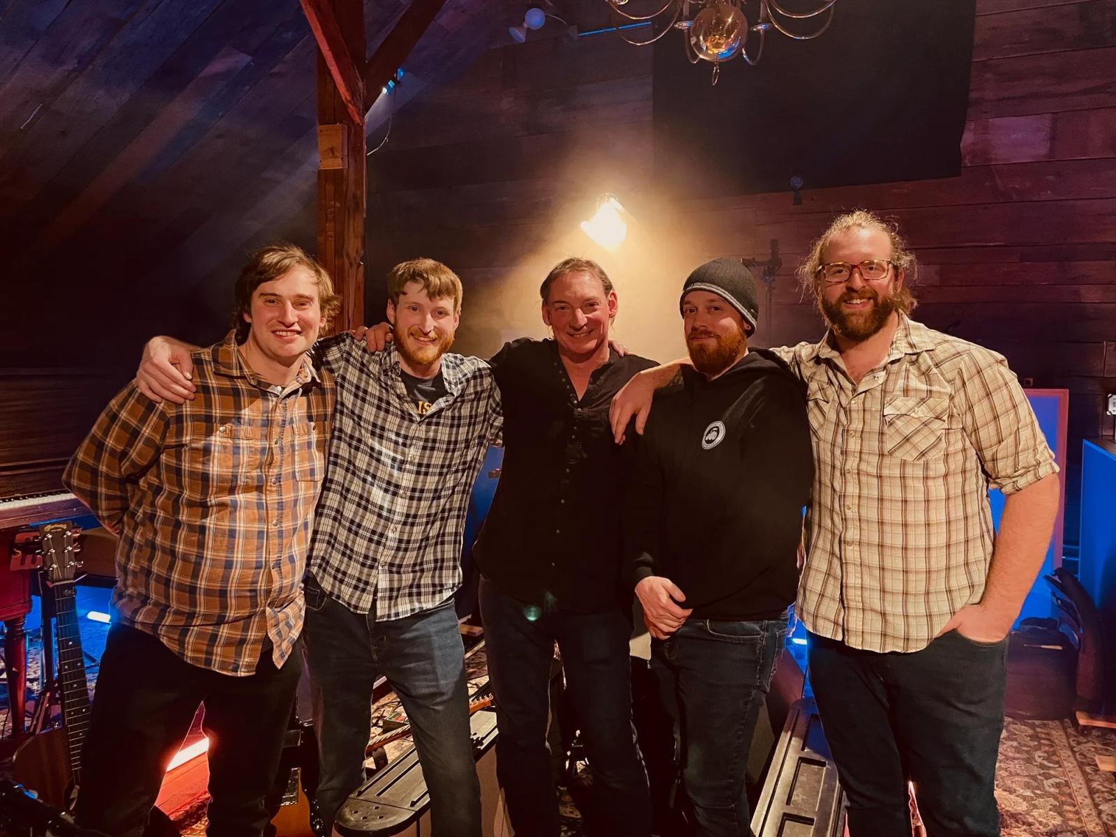 Five men smiling and standing together in a warmly lit room.