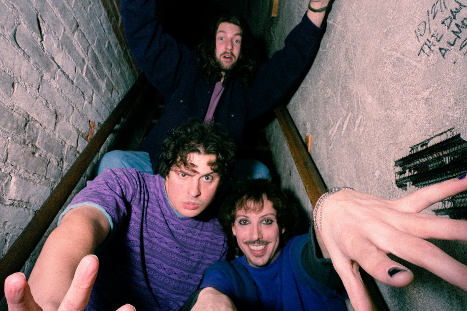 Three people posing playfully on narrow stairs, arms reaching towards the camera.