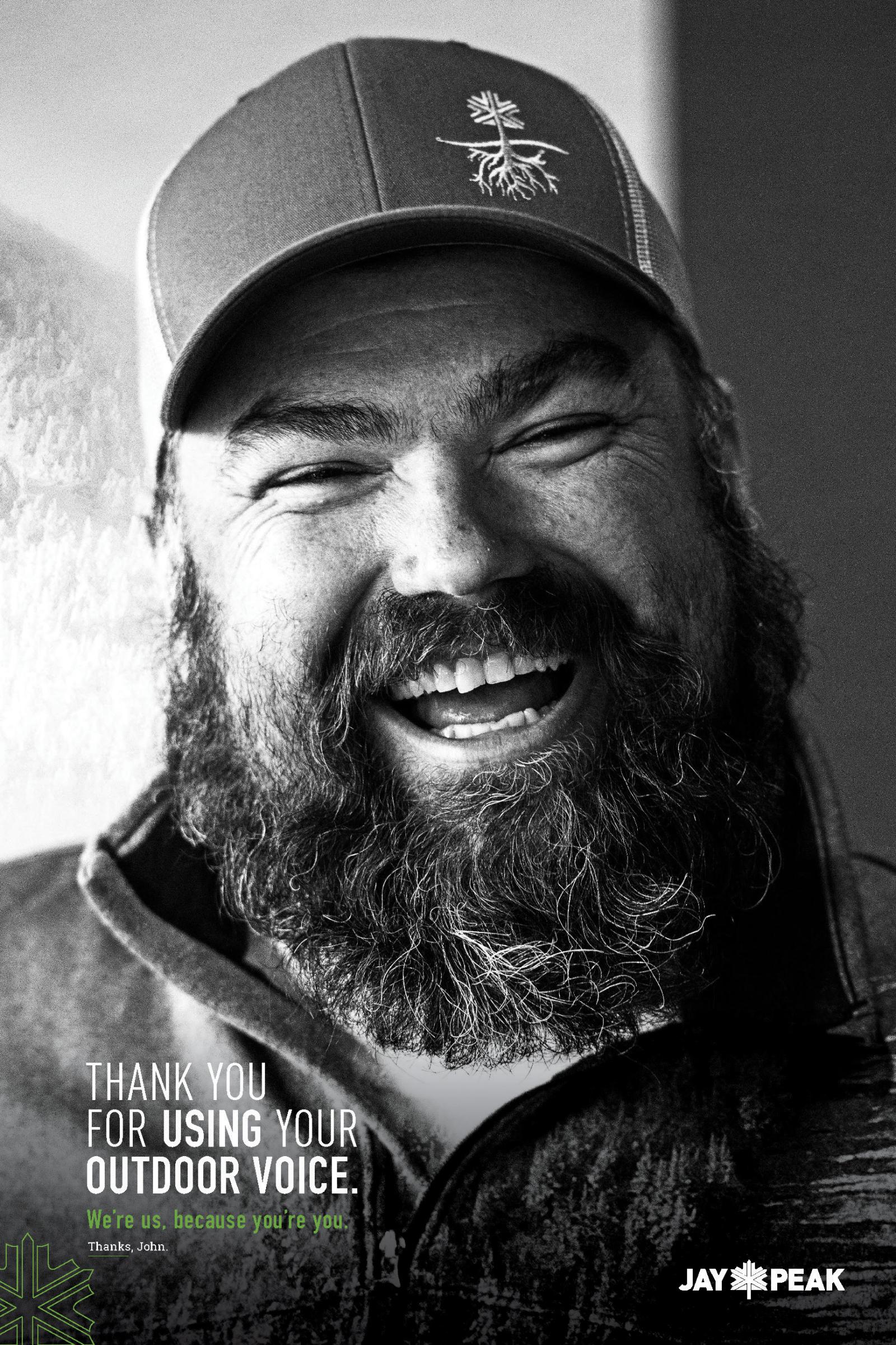 Smiling man with a beard wearing a cap, in black and white.