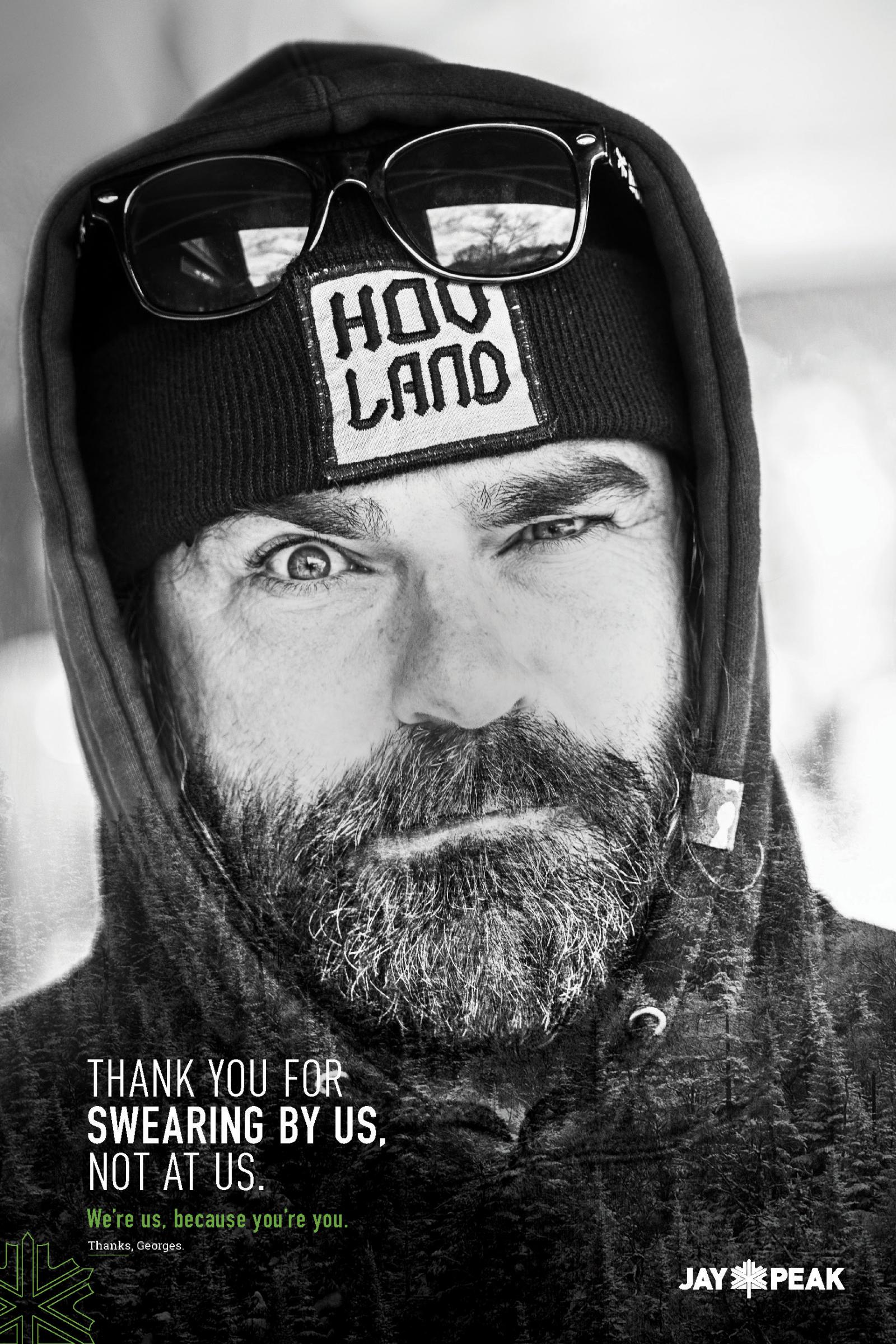 Man with a beanie and glasses winks, wearing a hoodie, in black and white.