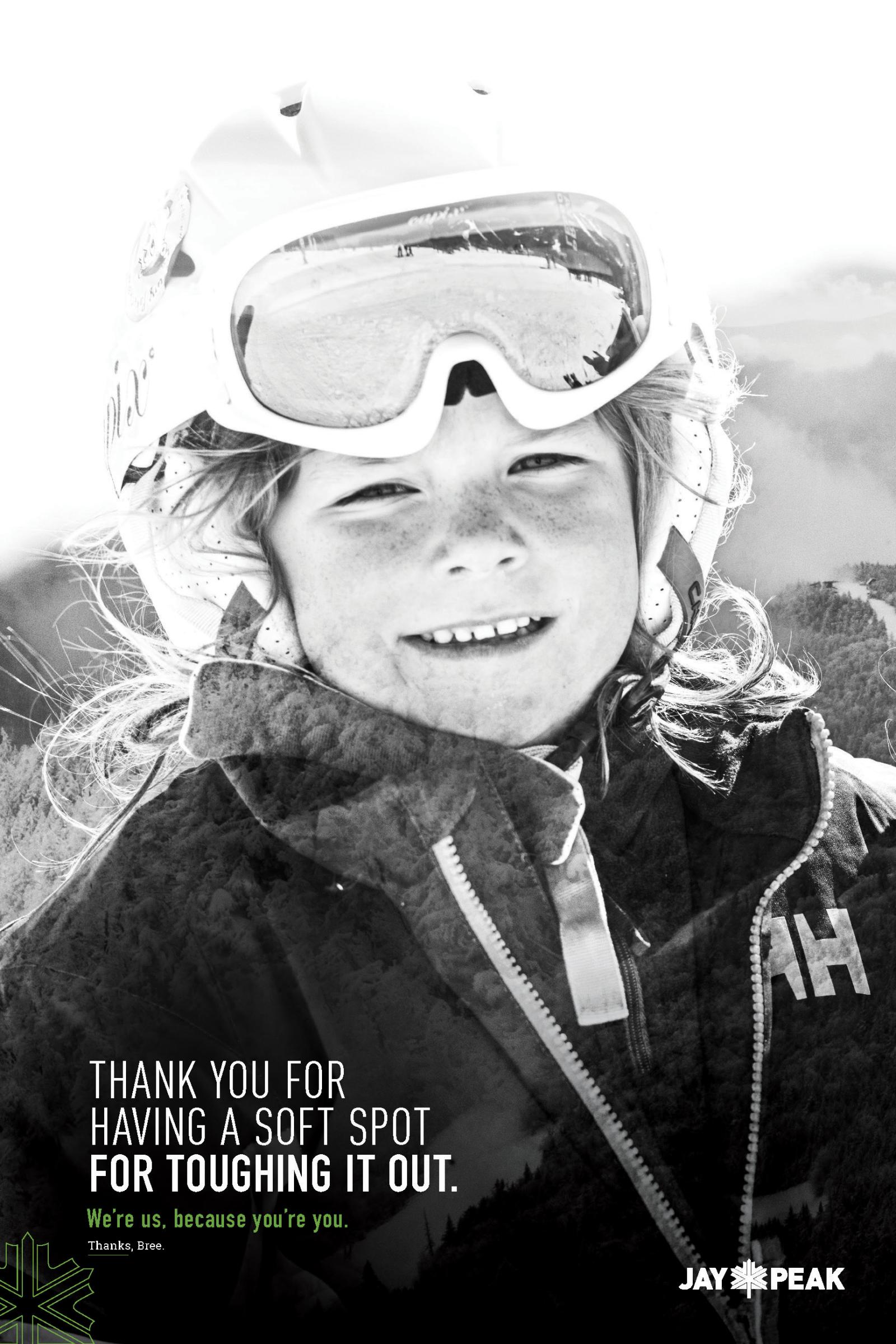 Smiling child in ski gear with snowy mountains in the background, black and white photo.