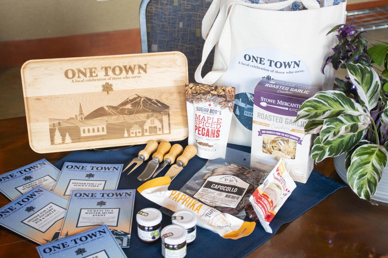 Gift items on a table, including a tote, cutting board, snacks, and plant.