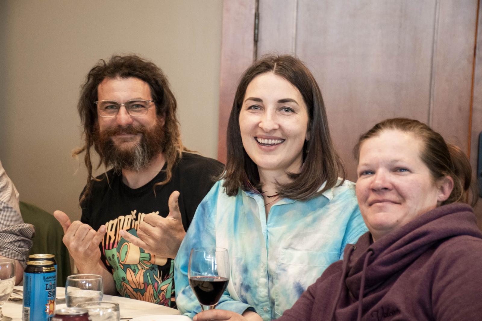 Three people smiling at a table, with drinks and a relaxed atmosphere.