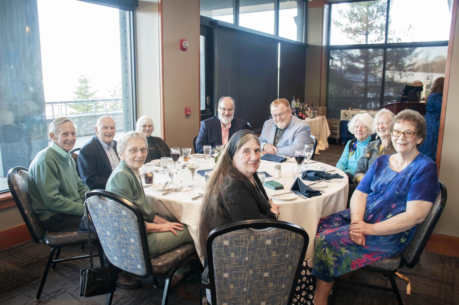 Elderly group seated at a round table, smiling in a well-lit dining area.