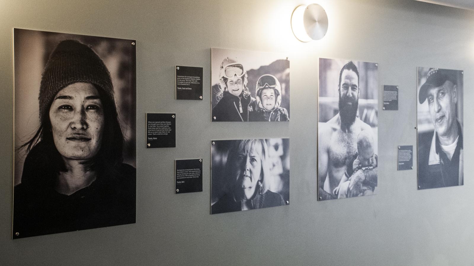 Black-and-white photo gallery with portraits on a gray wall, softly lit by overhead lights.