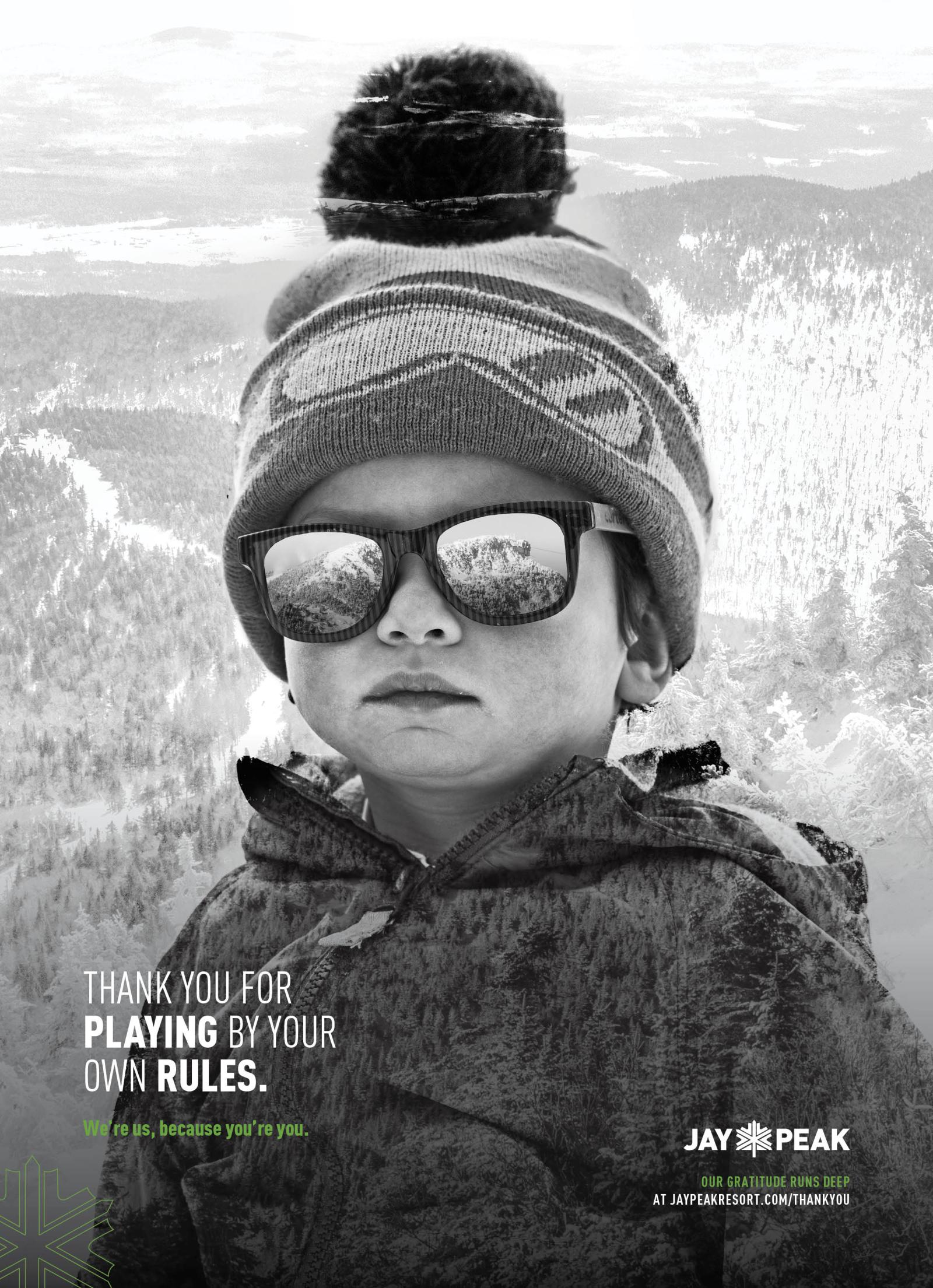 Young child in winter gear with sunglasses, snowy landscape in background. Black and white photo.