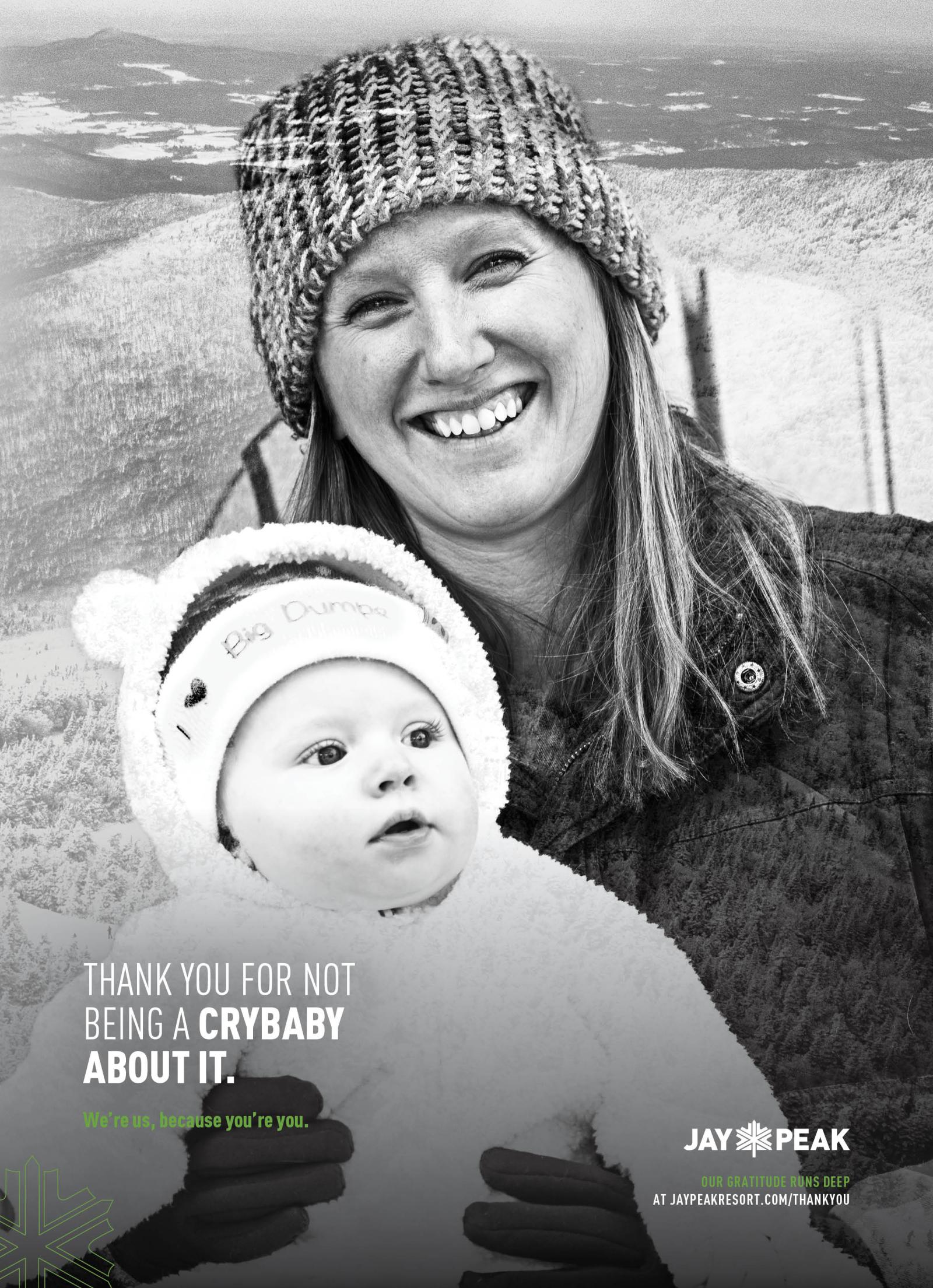 Smiling woman with baby in winter clothing, snowy mountain background. Black and white photo.