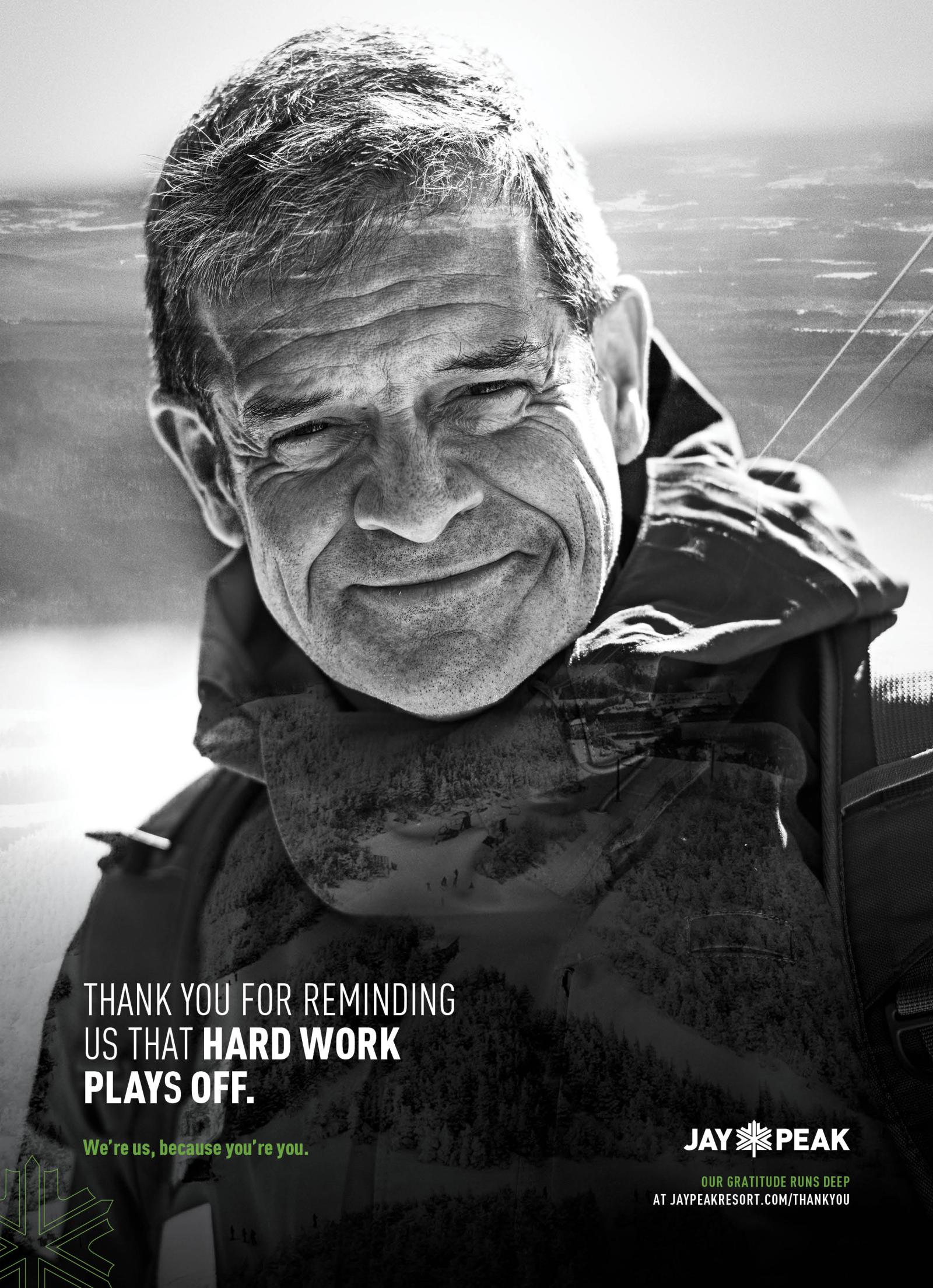 Smiling man in outdoor gear, black and white photo, mountainous background.