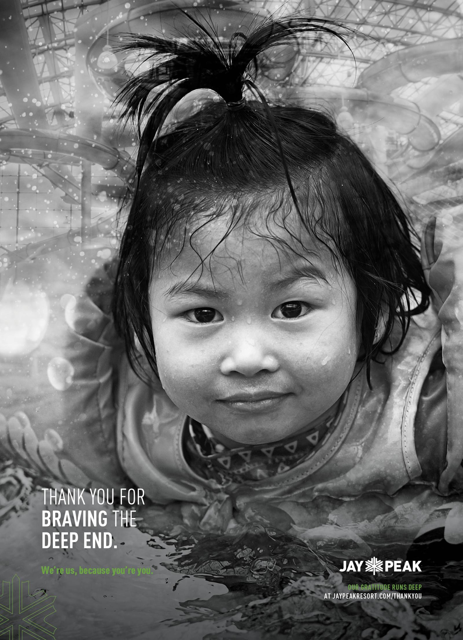 Young child in water, smiling, with hair tied up, black-and-white photograph.