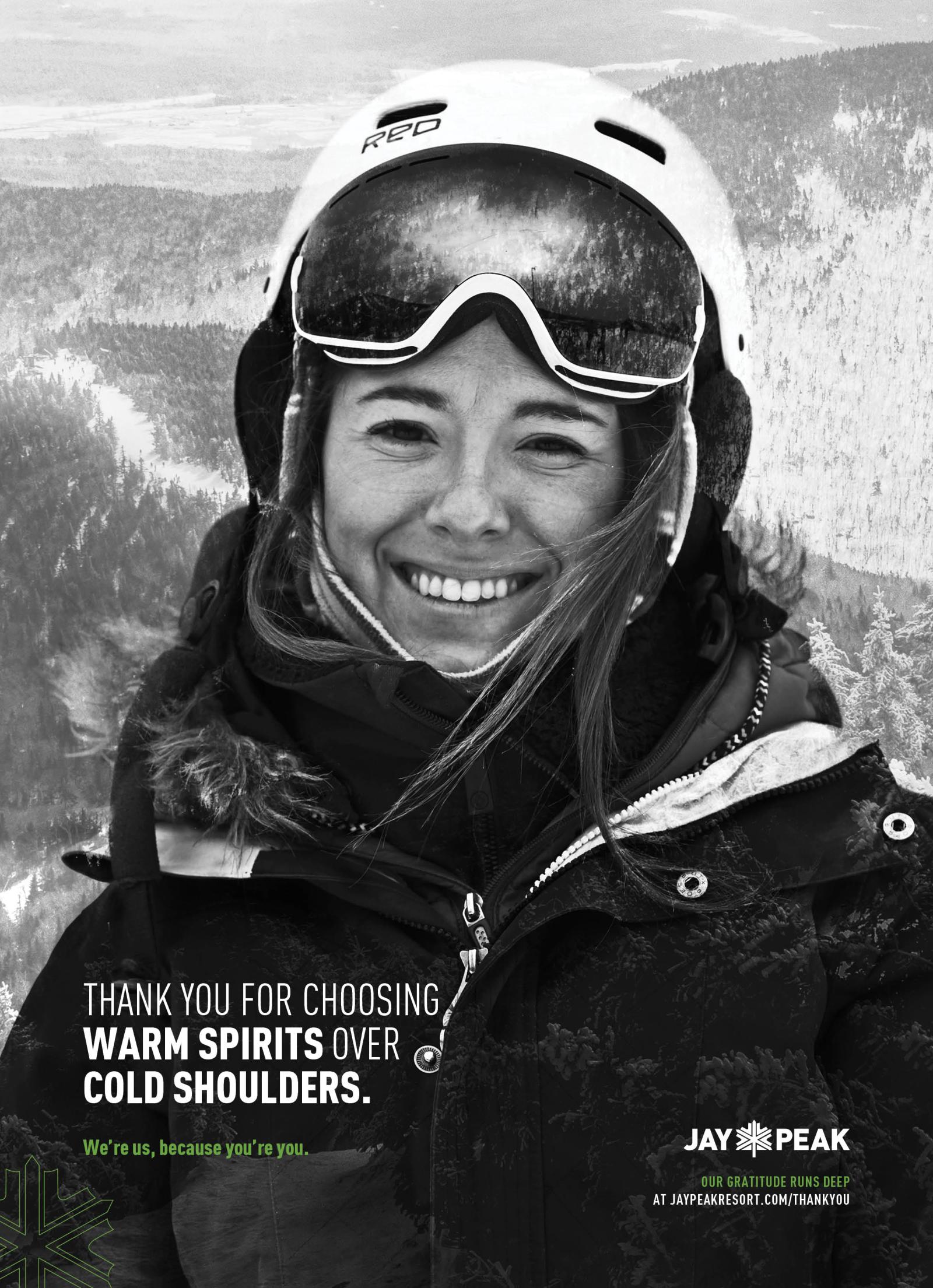 Black and white photo of a woman smiling in ski gear, snowy mountains behind.