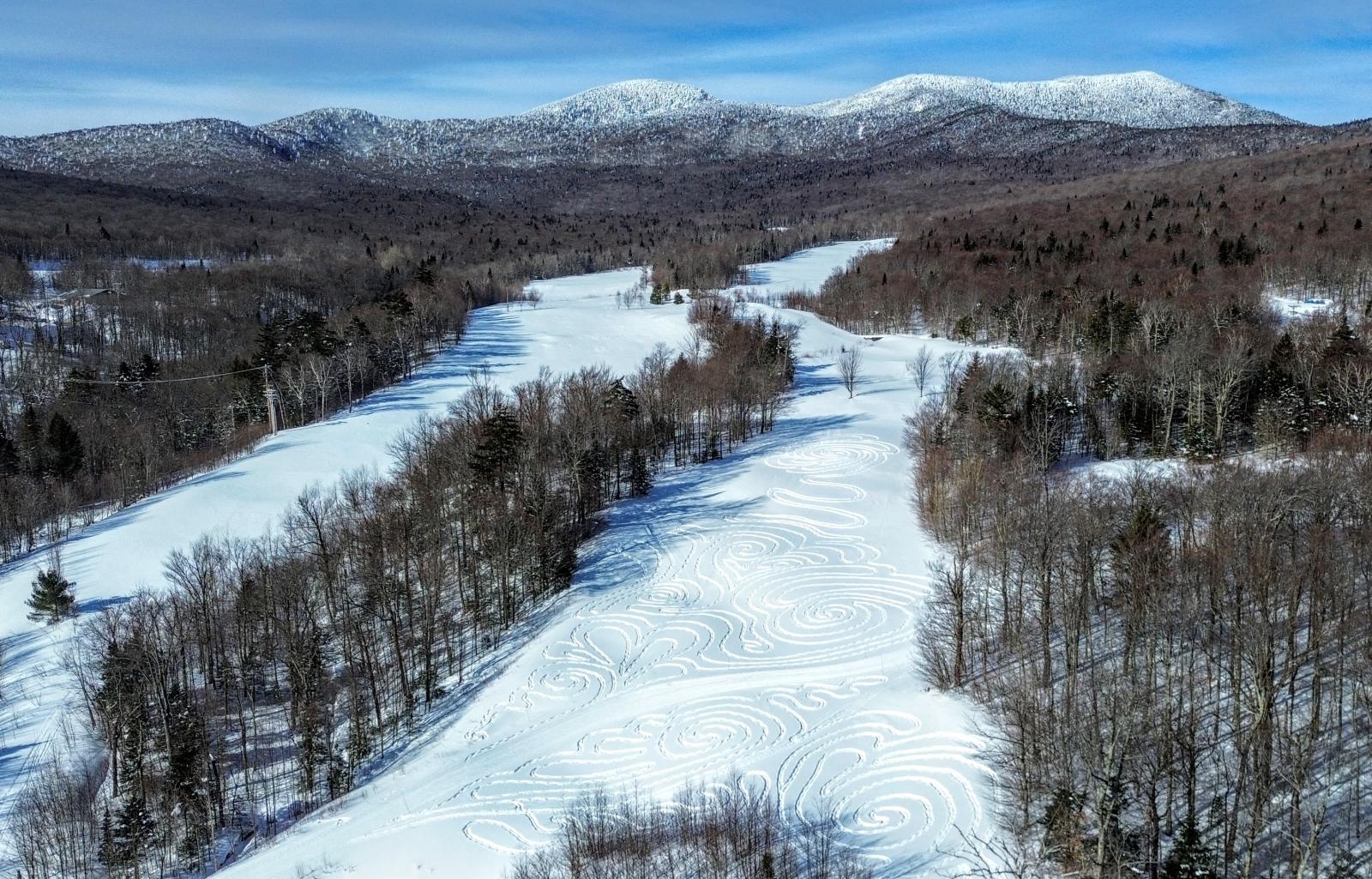 Snow-covered landscape with mountains in the background under a clear blue sky.