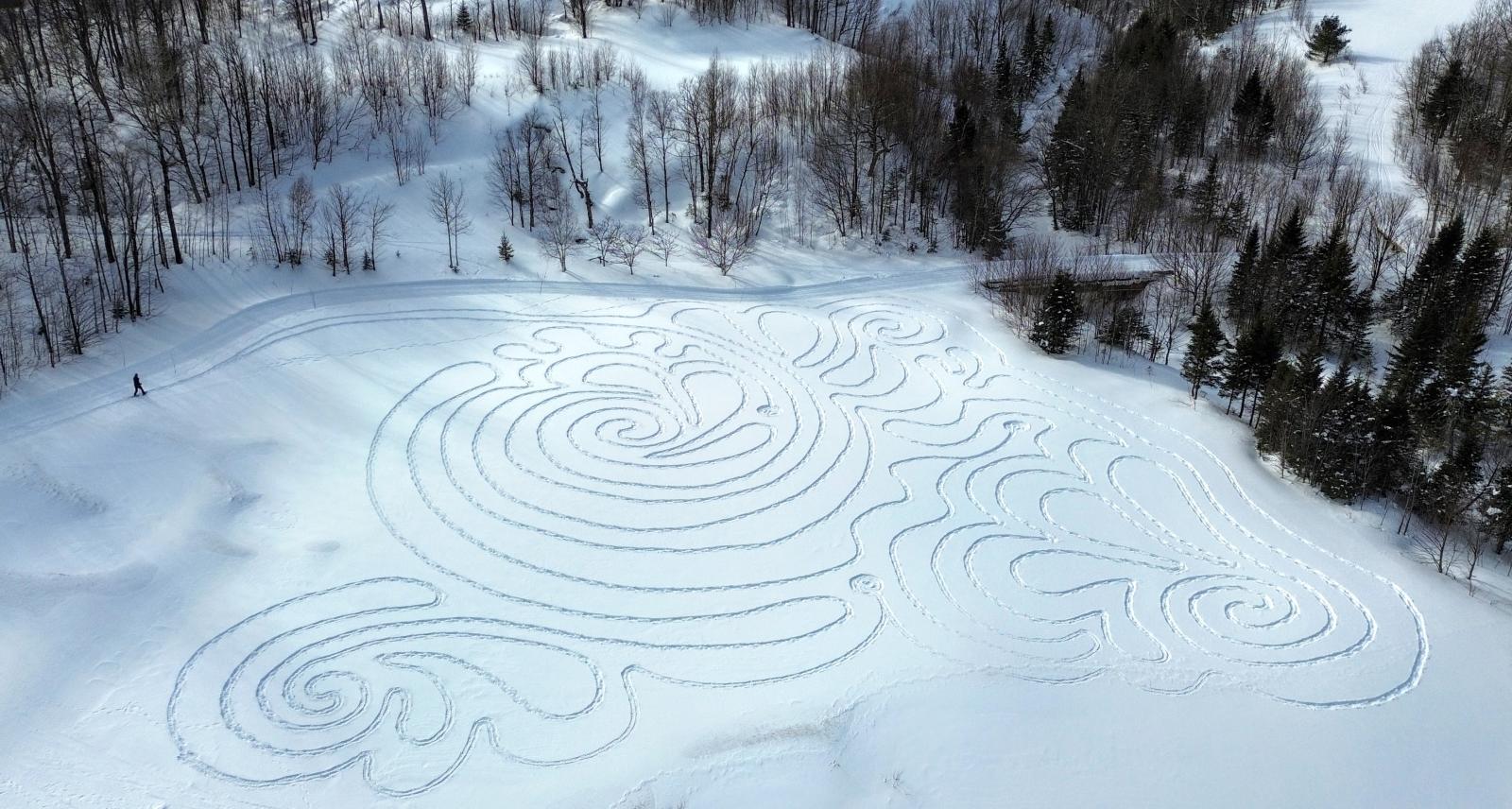 Snow labyrinth with intricate swirling patterns surrounded by trees.