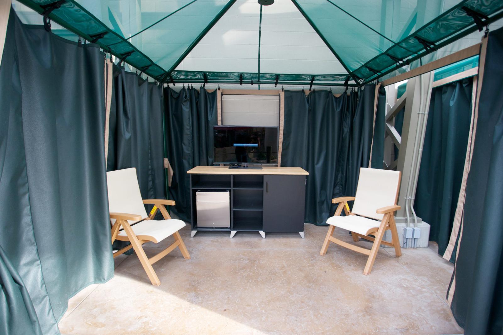 Outdoor cabana with two chairs and a cabinet under teal canopy.