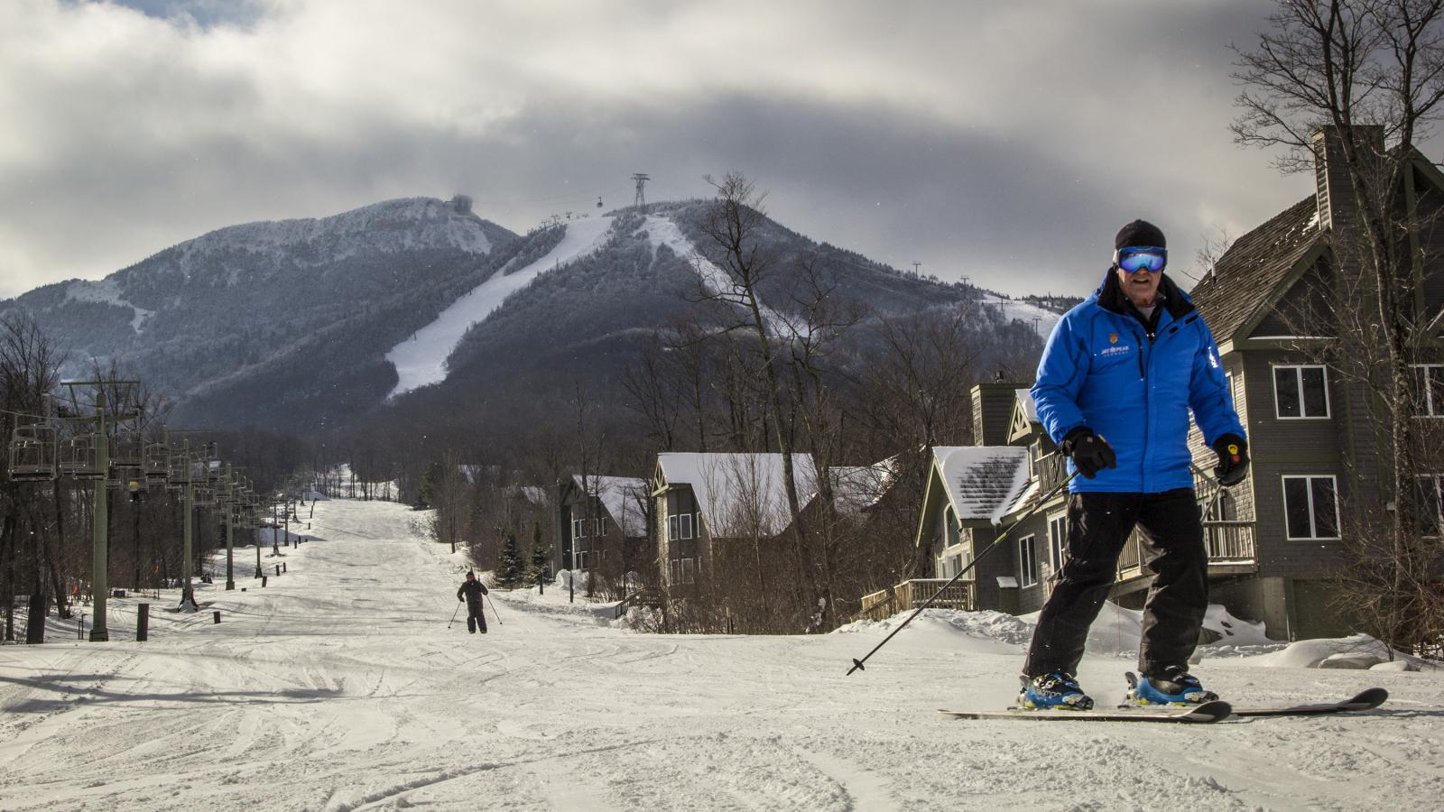 Skier in blue jacket on snowy mountain slope, cloudy sky above.