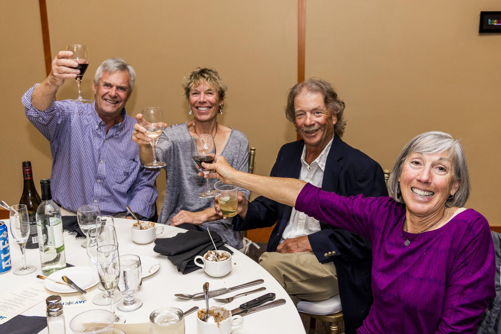 Four people smiling and toasting with wine at a round table.