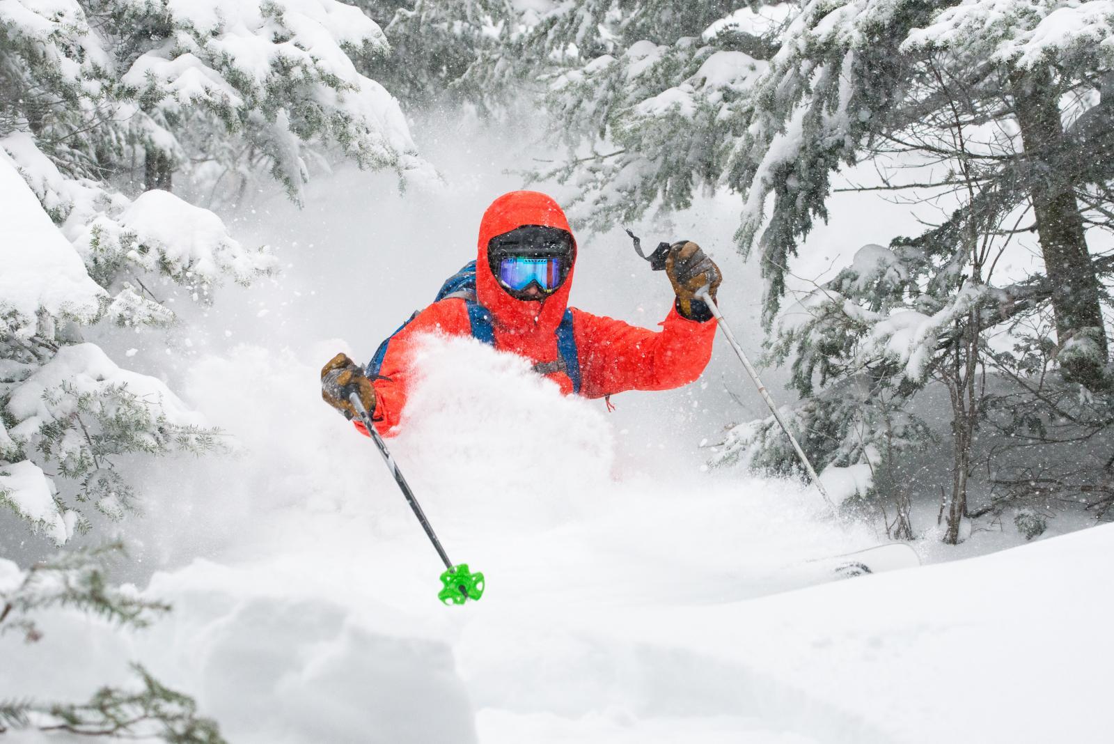 Skiing through fresh snow in a snowy forest, wearing a red jacket and goggles.