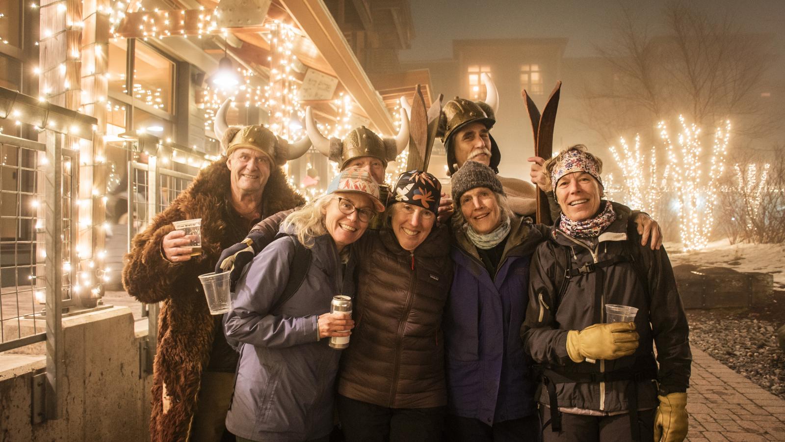 Friends in festive outfits smile together amid holiday lights at night.
