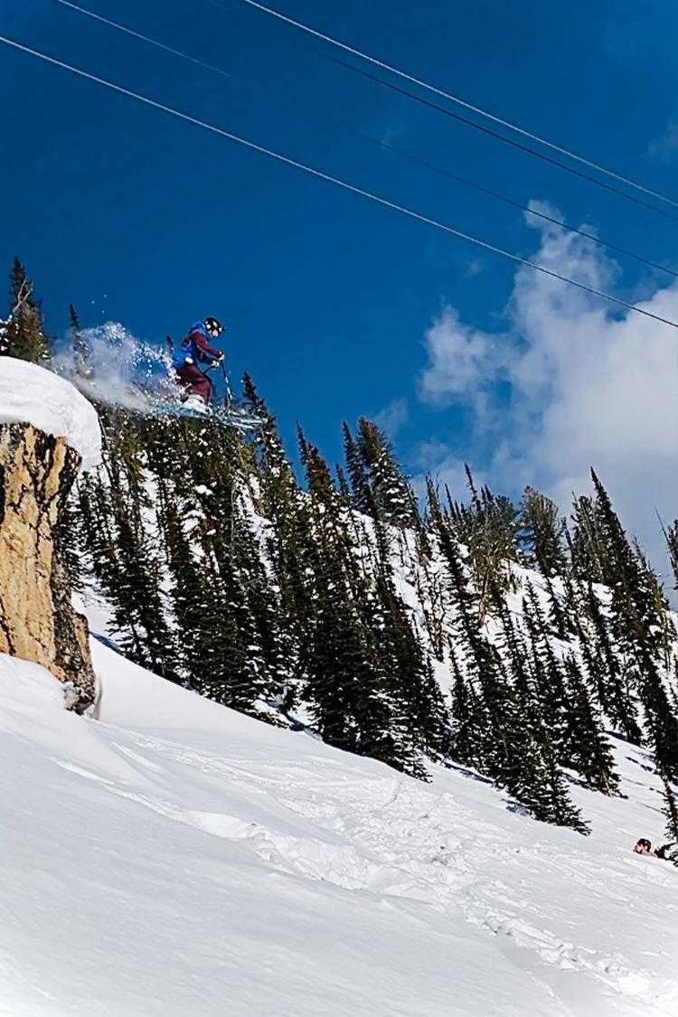 Skier jumping off a snowy cliff, vibrant blue sky above.