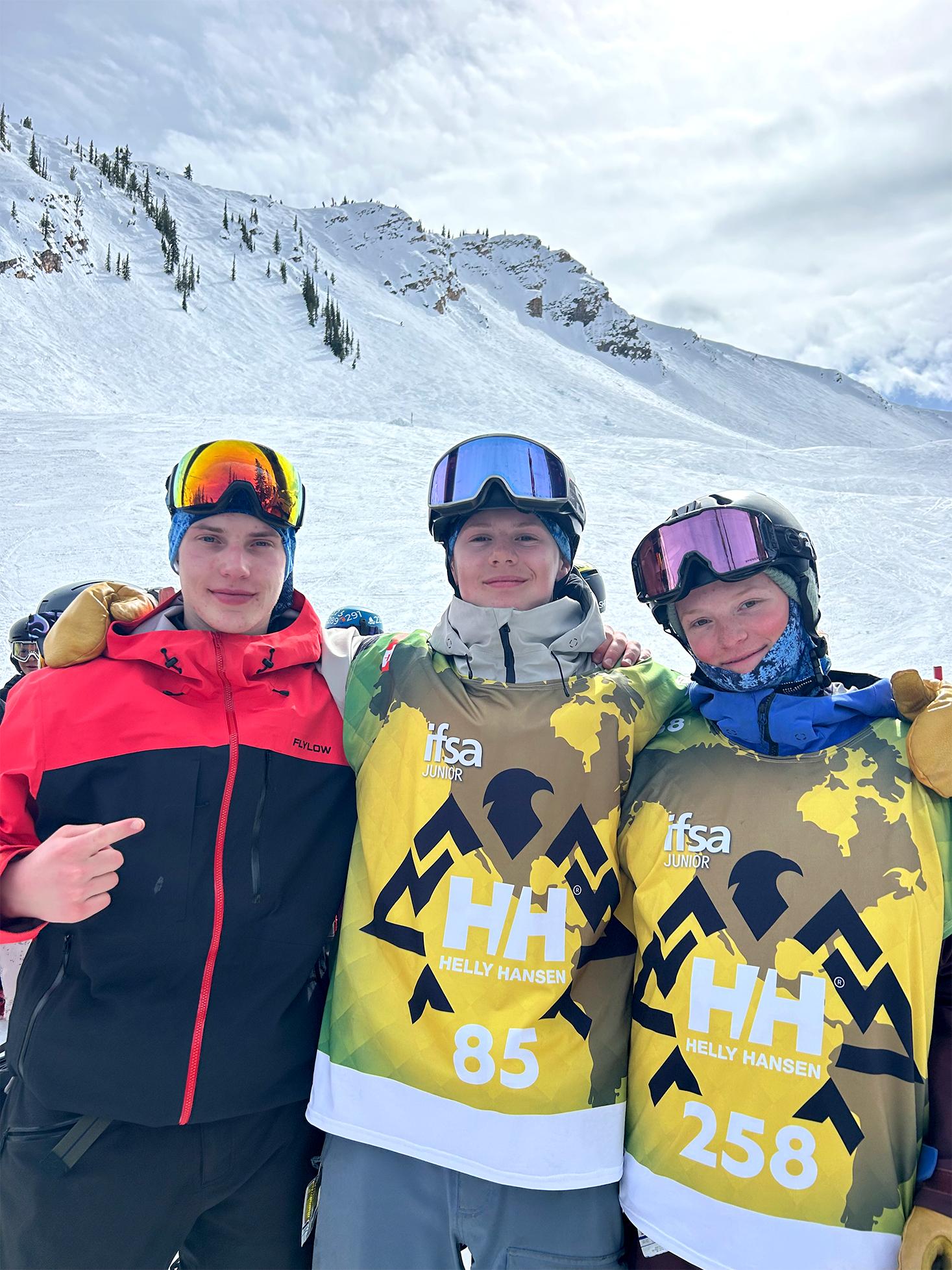 Three skiers in gear pose together on a snowy mountain.