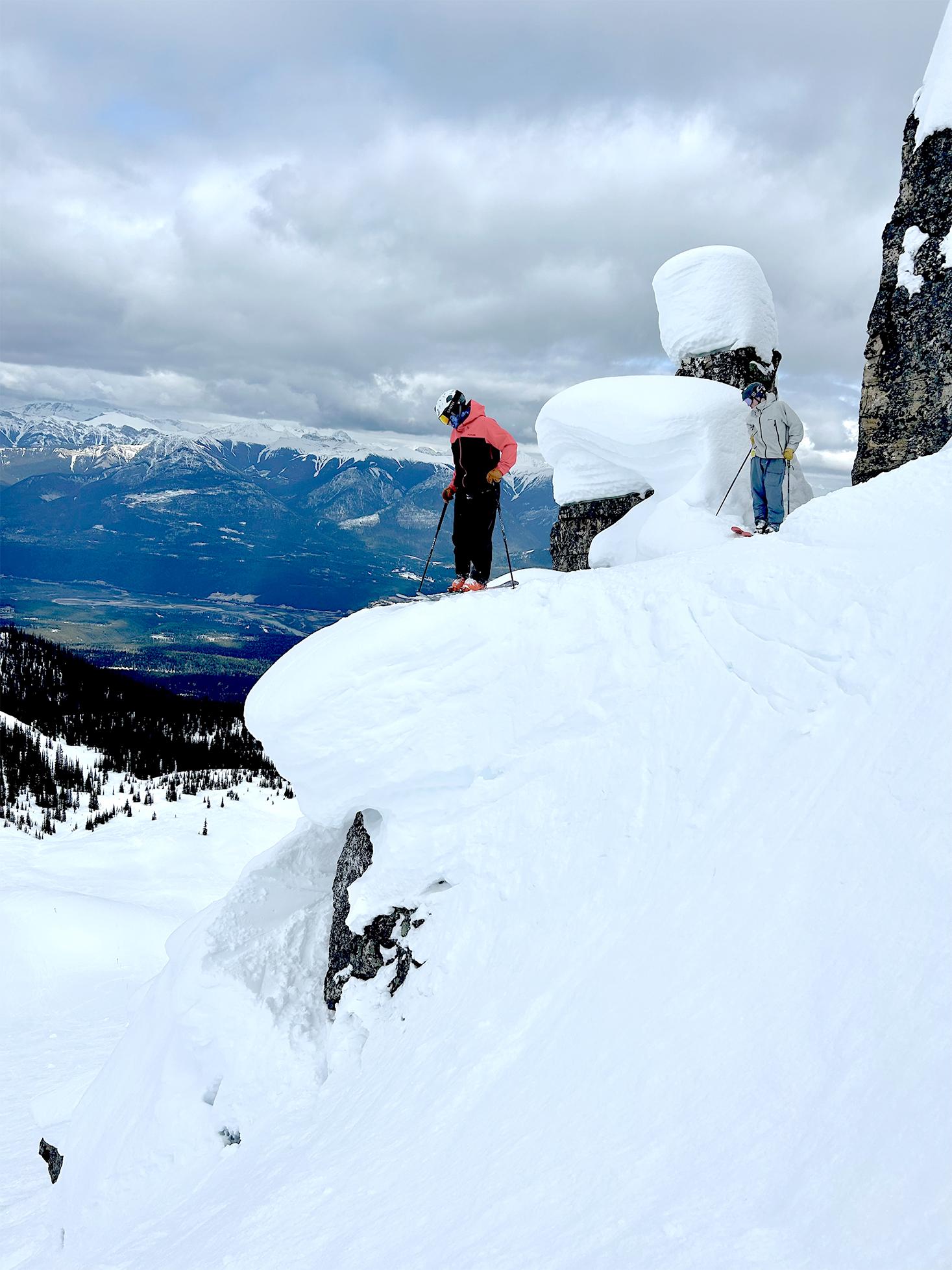 Snowy mountain peak with skiers, cloudy sky in the background.