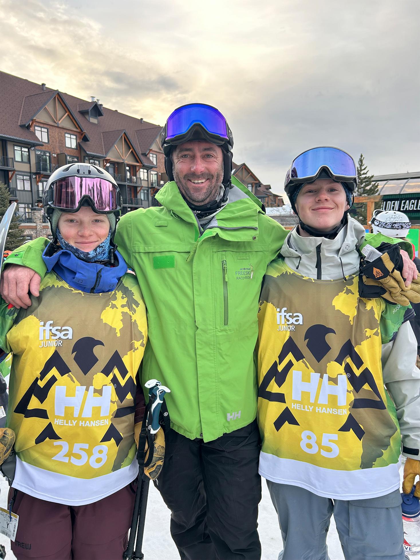 Three skiers in helmets and goggles, smiling in a snowy resort.