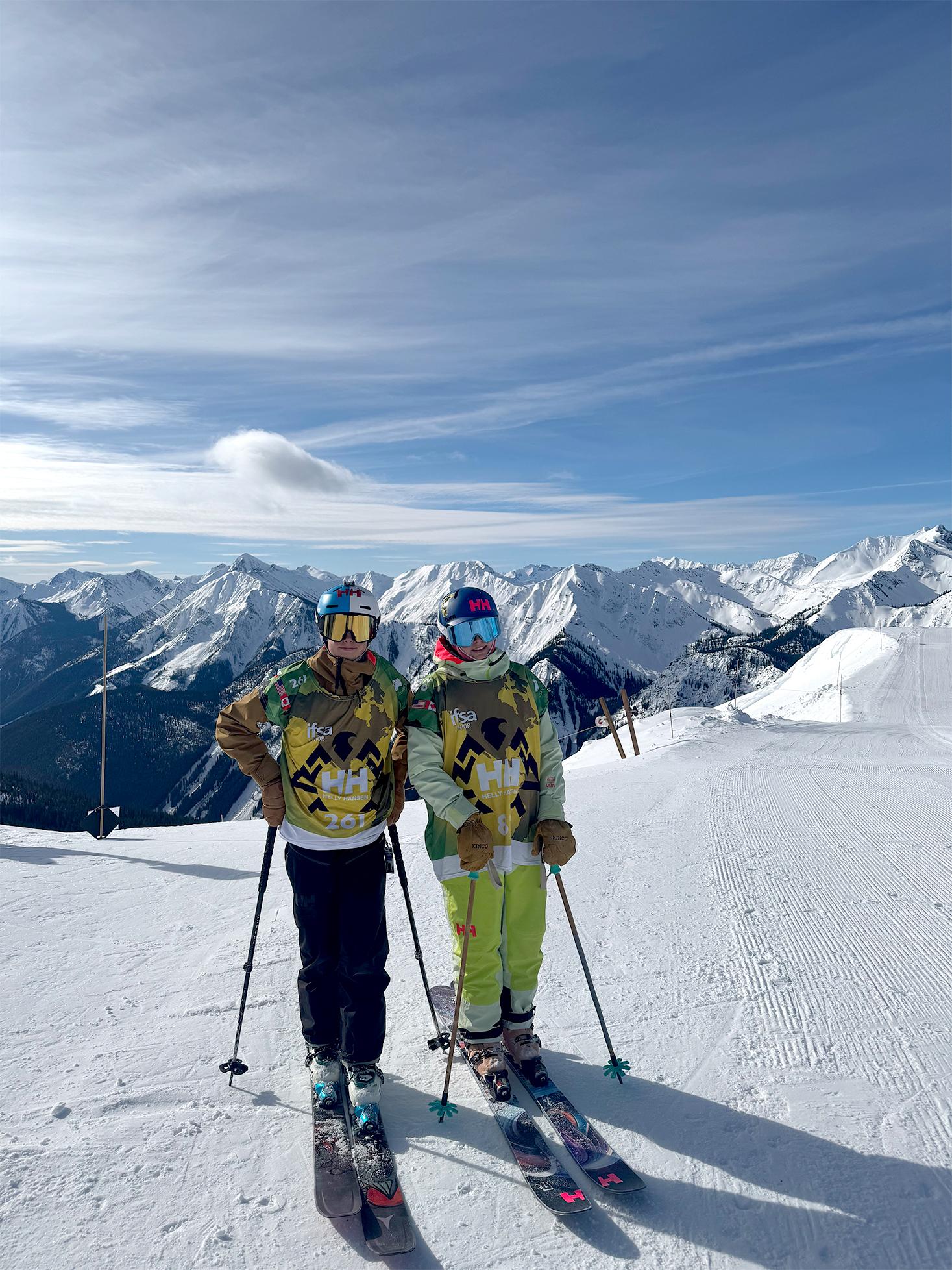Two skiers in colorful outfits on a snowy mountain with a clear sky background.